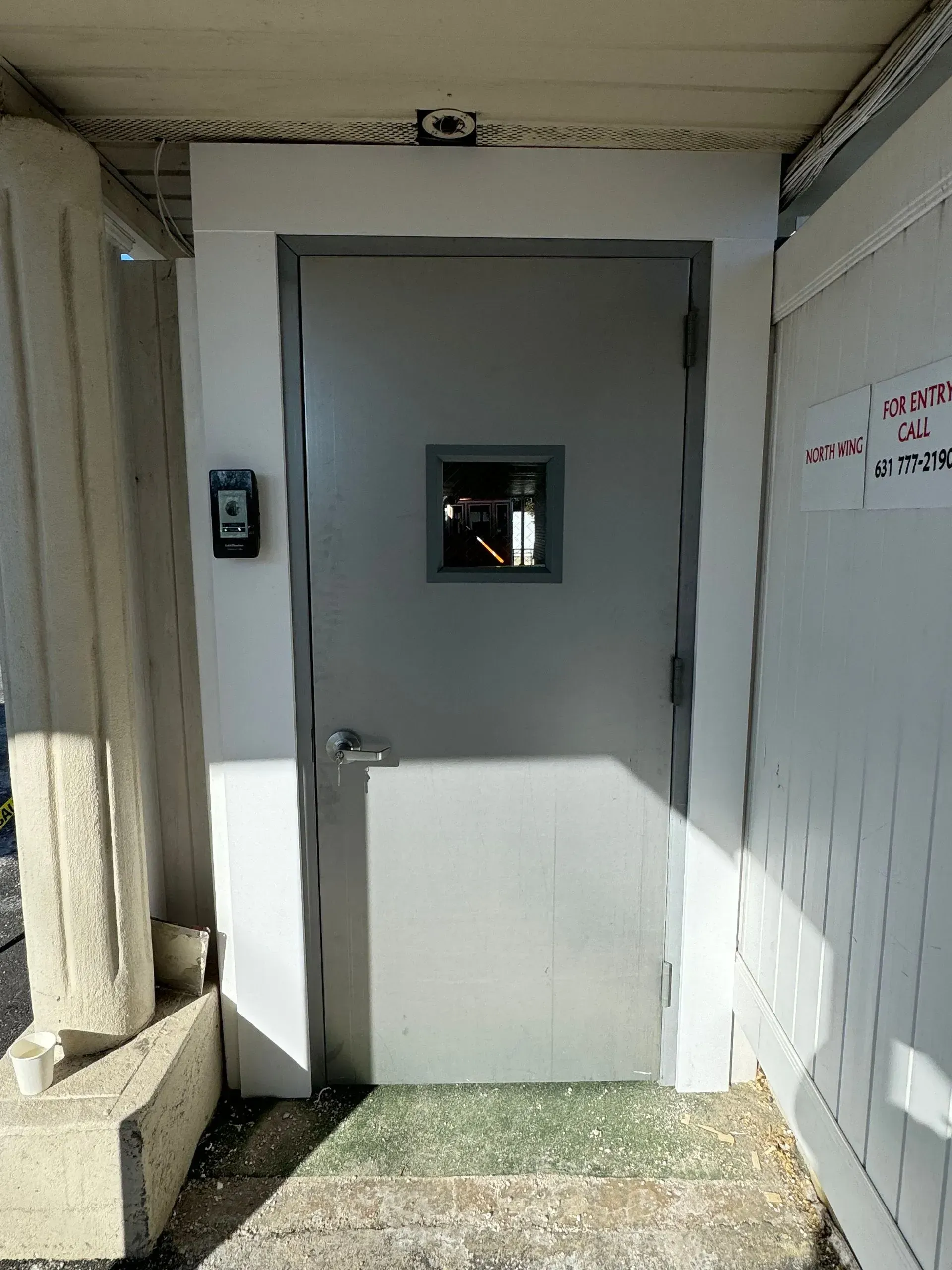 Gray door with small window, access control panel, and green doormat.