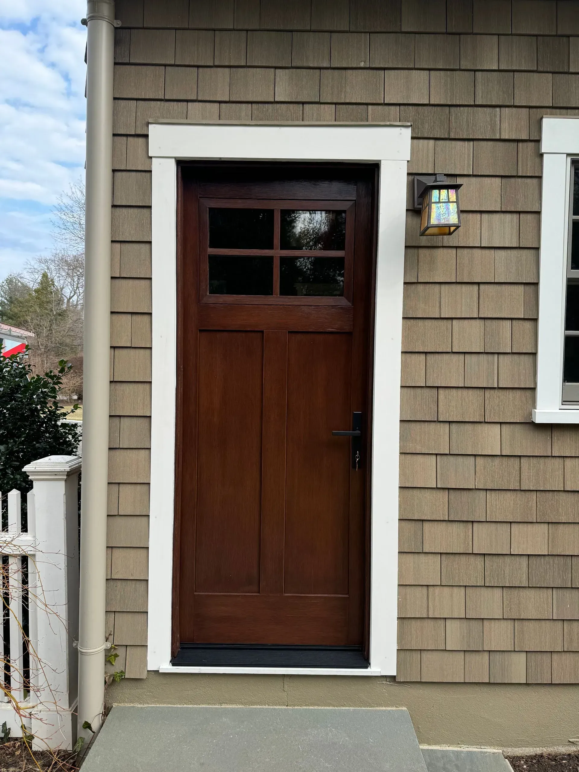 Brown door with white trim, brown shingled wall, and a side window.