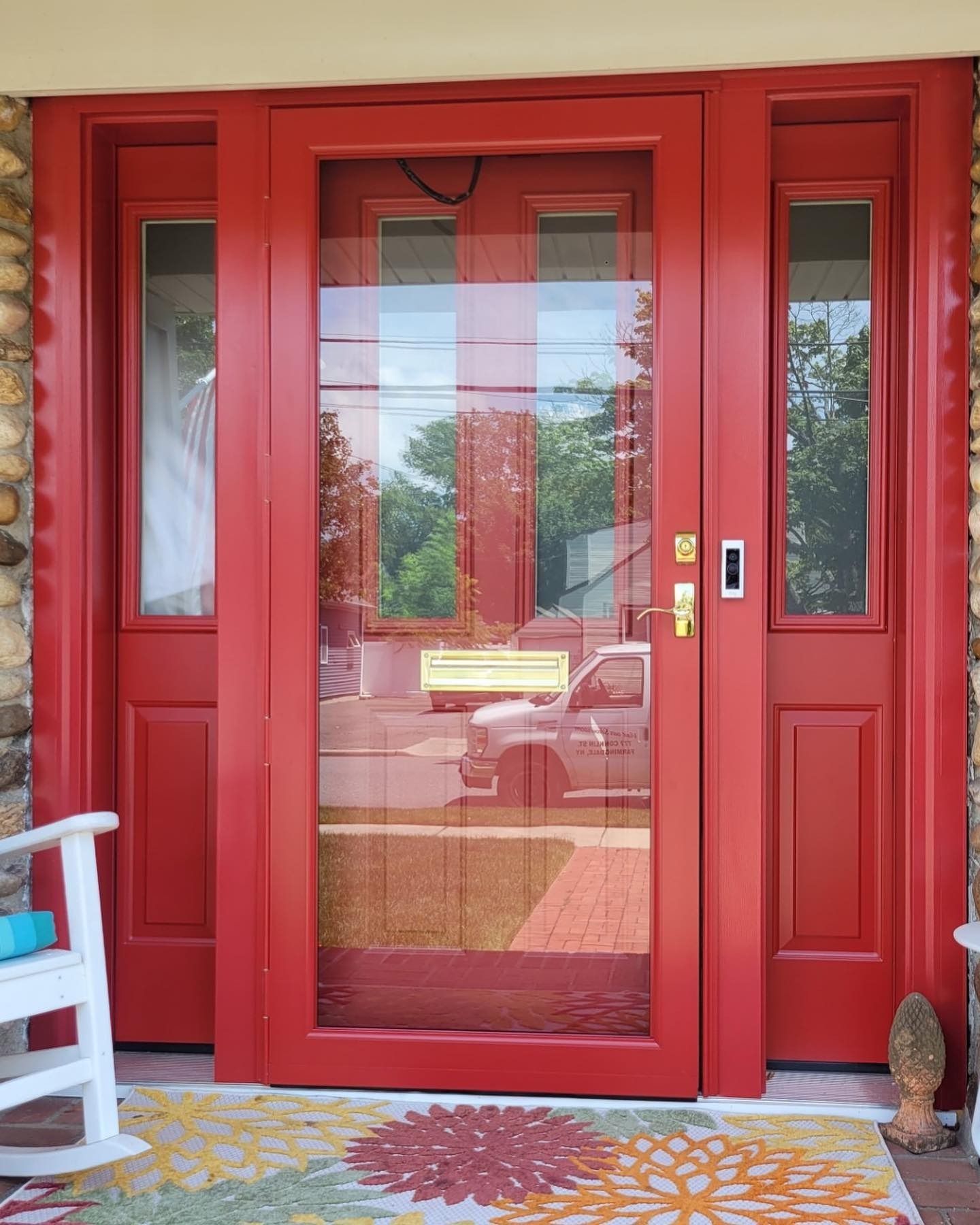 Red front door with sidelights, screen door, and colorful welcome mat.