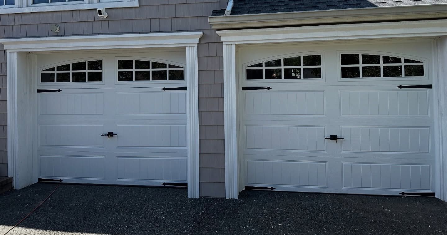 Two white garage doors with arched window panels and decorative black handles and hinges.
