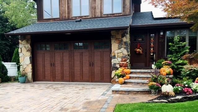 Brown house with stone accents, garage door, and fall decorations on steps.