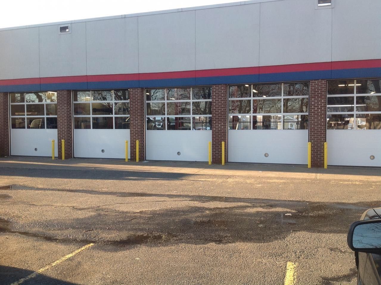 Exterior of a building with multiple white garage doors, brick columns, and a blue and red stripe across the top.