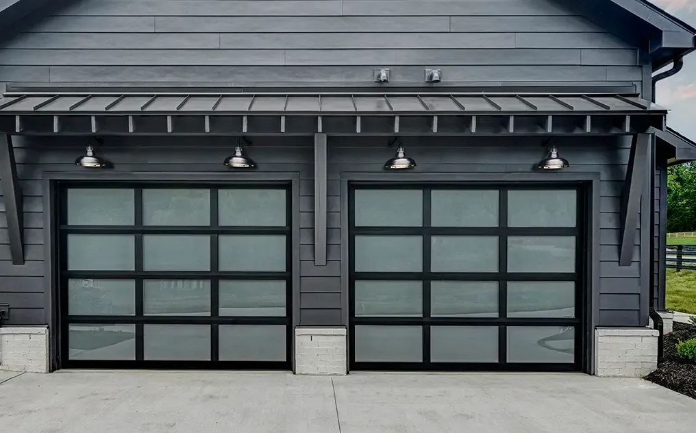 Two modern garage doors with black frames and frosted glass panels, gray exterior, overhead lighting.