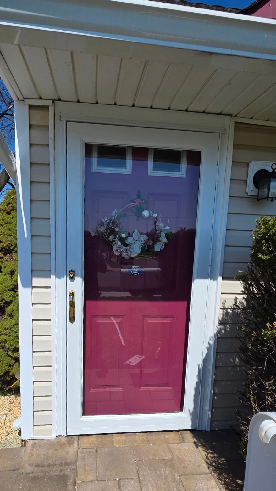 Front door with magenta lower panel, white trim, and floral wreath under a porch overhang.