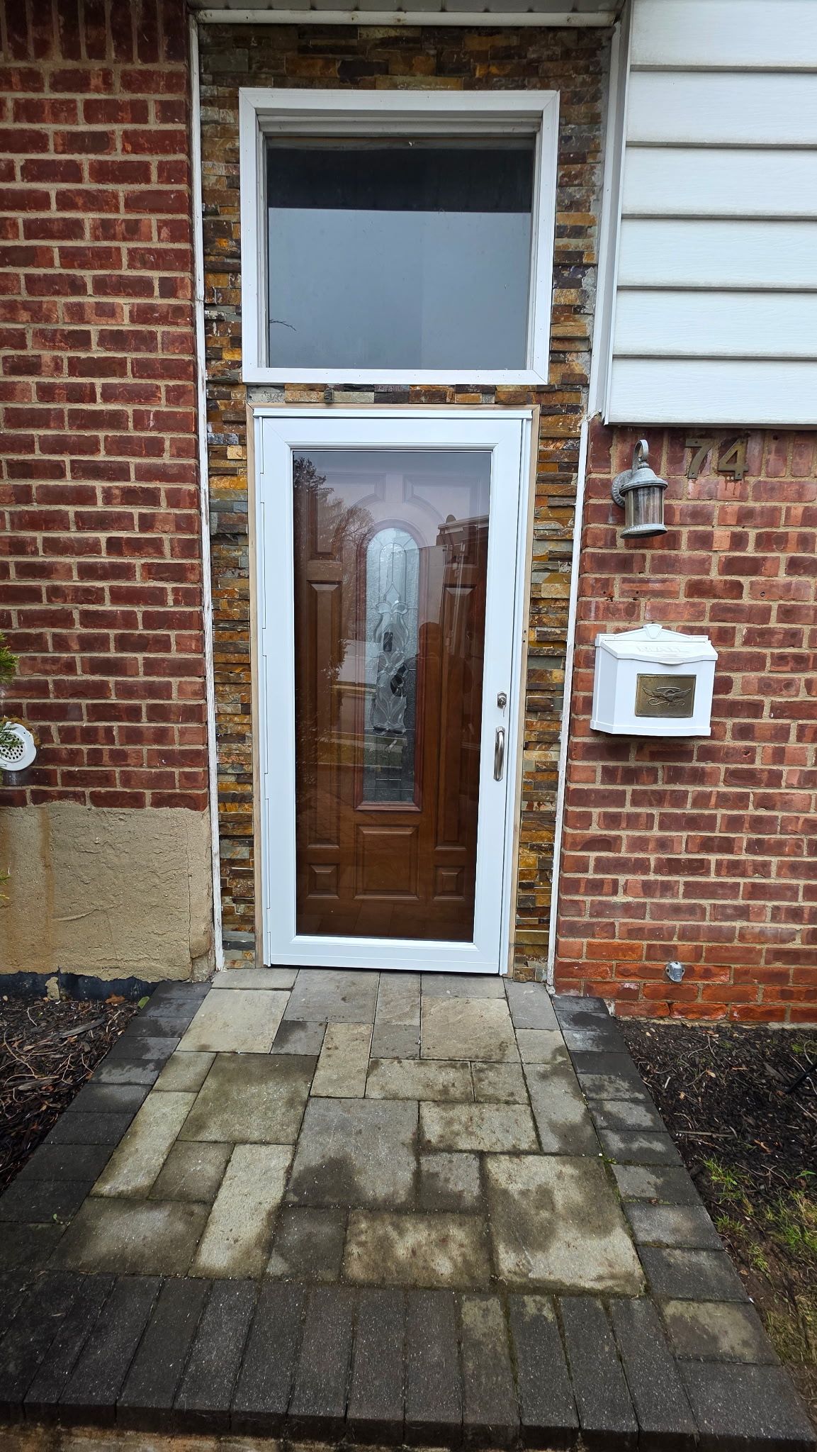 Front brick house entrance with a glass door, small stoop, and mailbox beside it