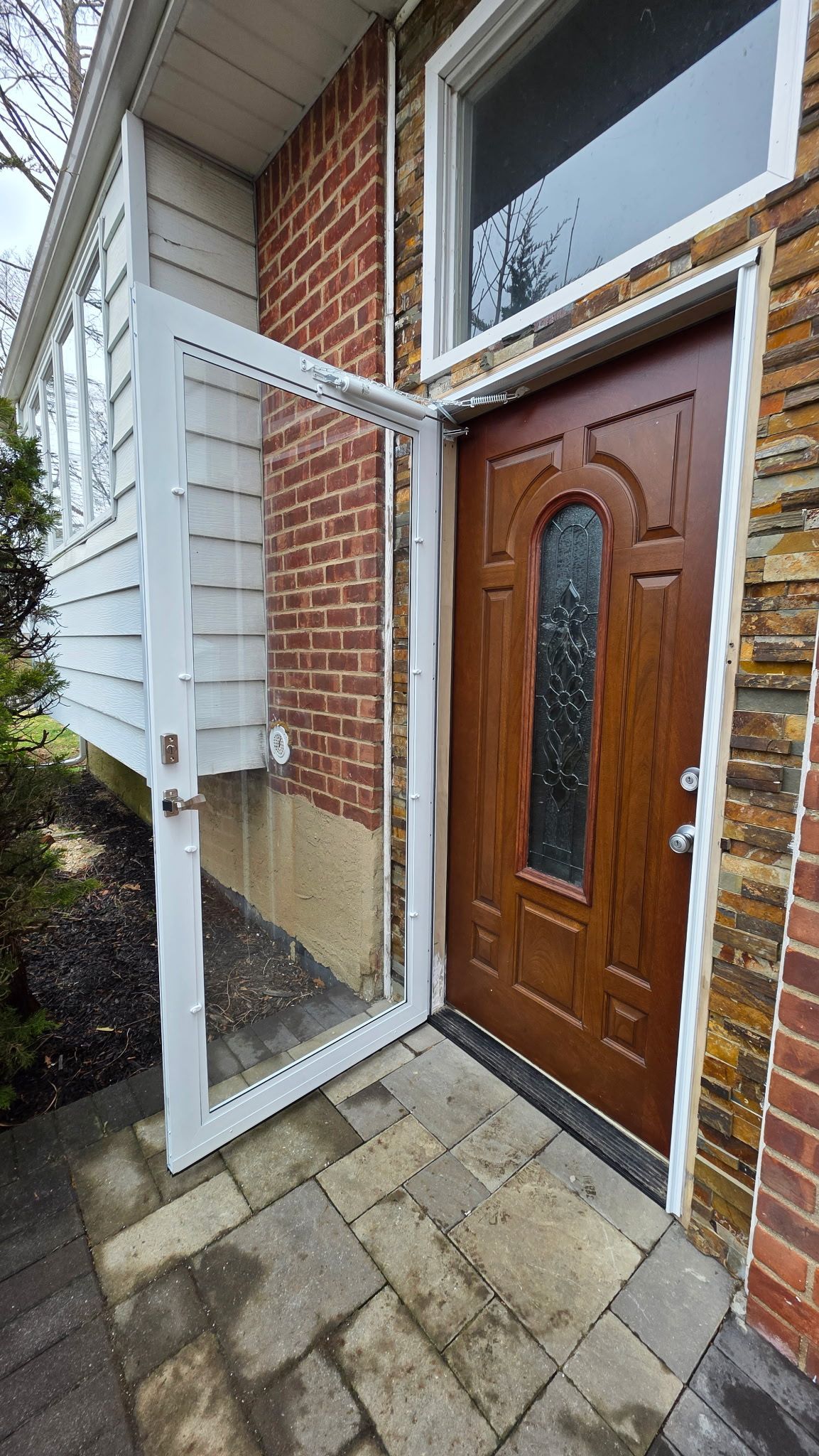 Open front door with glass panels beside brick and siding entryway on a paved porch