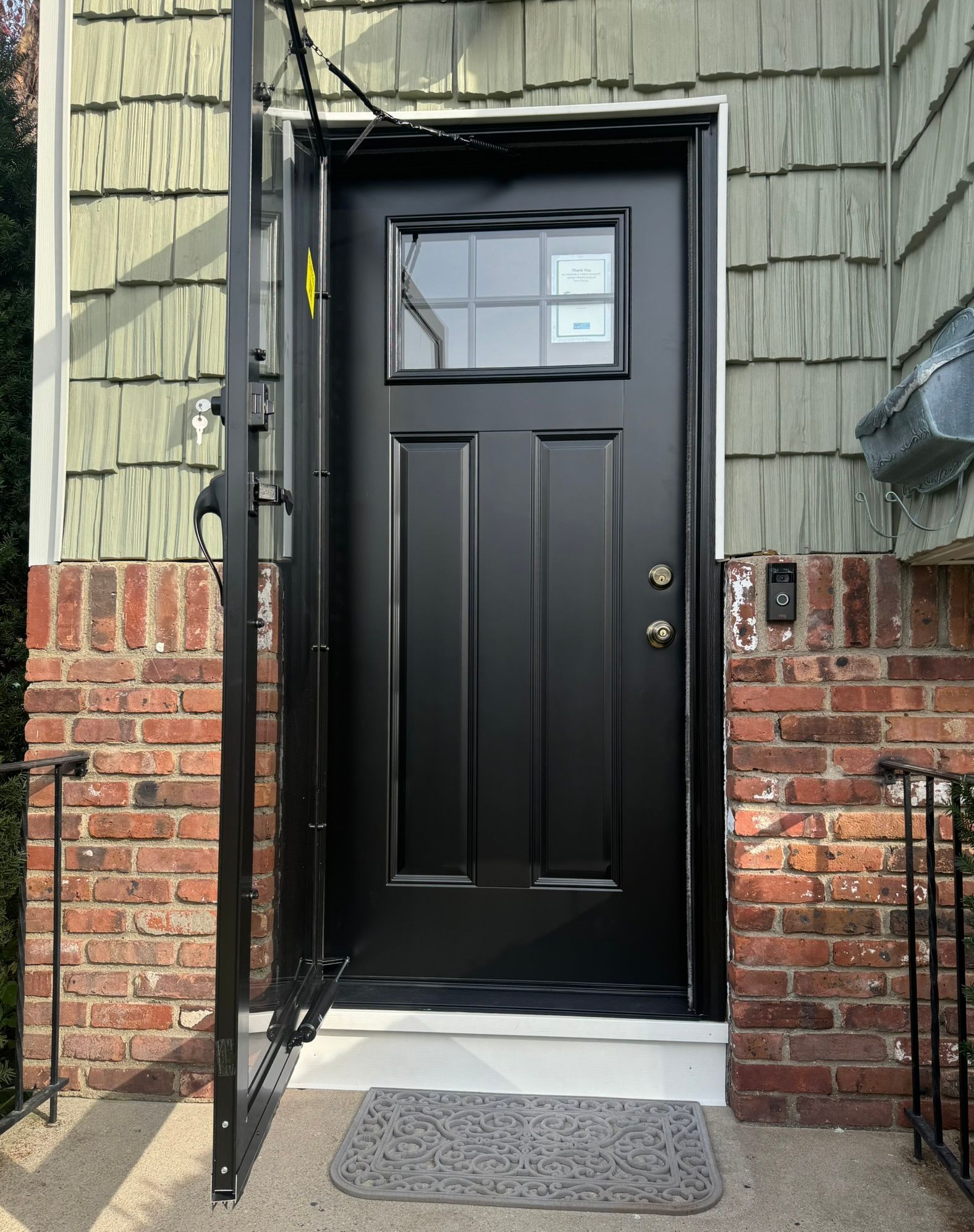 Black front door with small window, brick exterior, and open screen door on a house entryway.