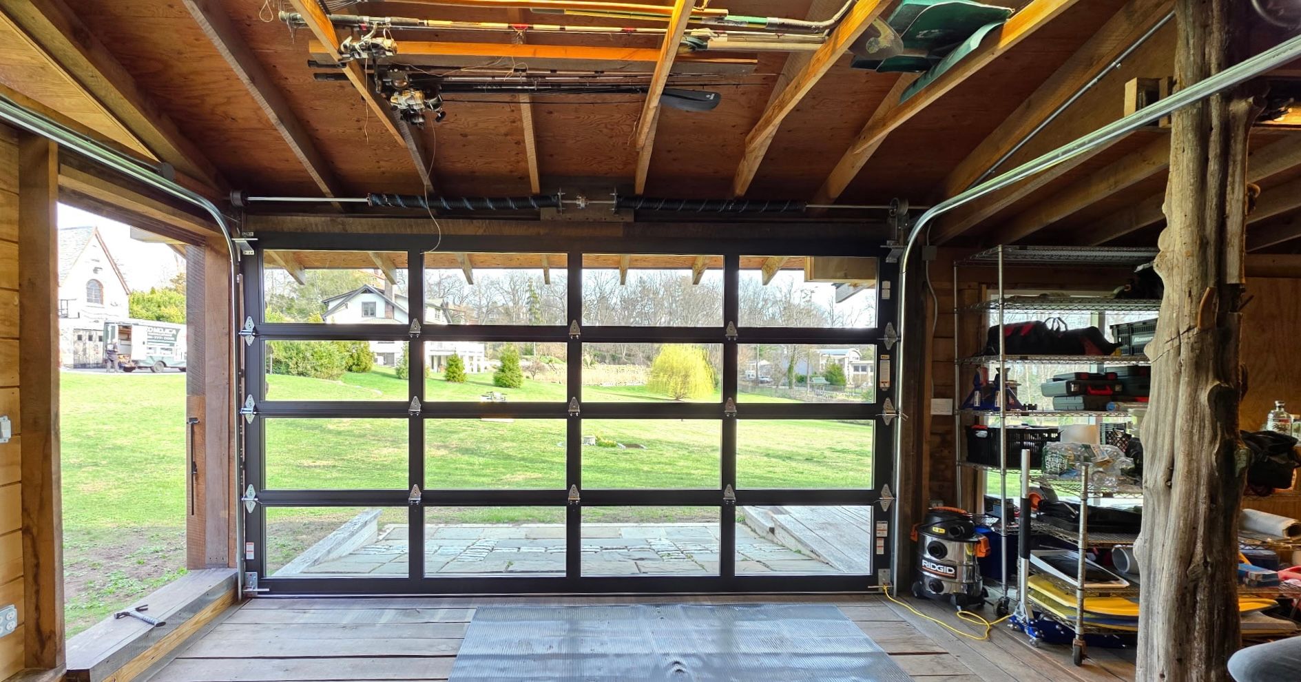 Garage interior with open glass door, wooden beams, and shelves of tools and supplies