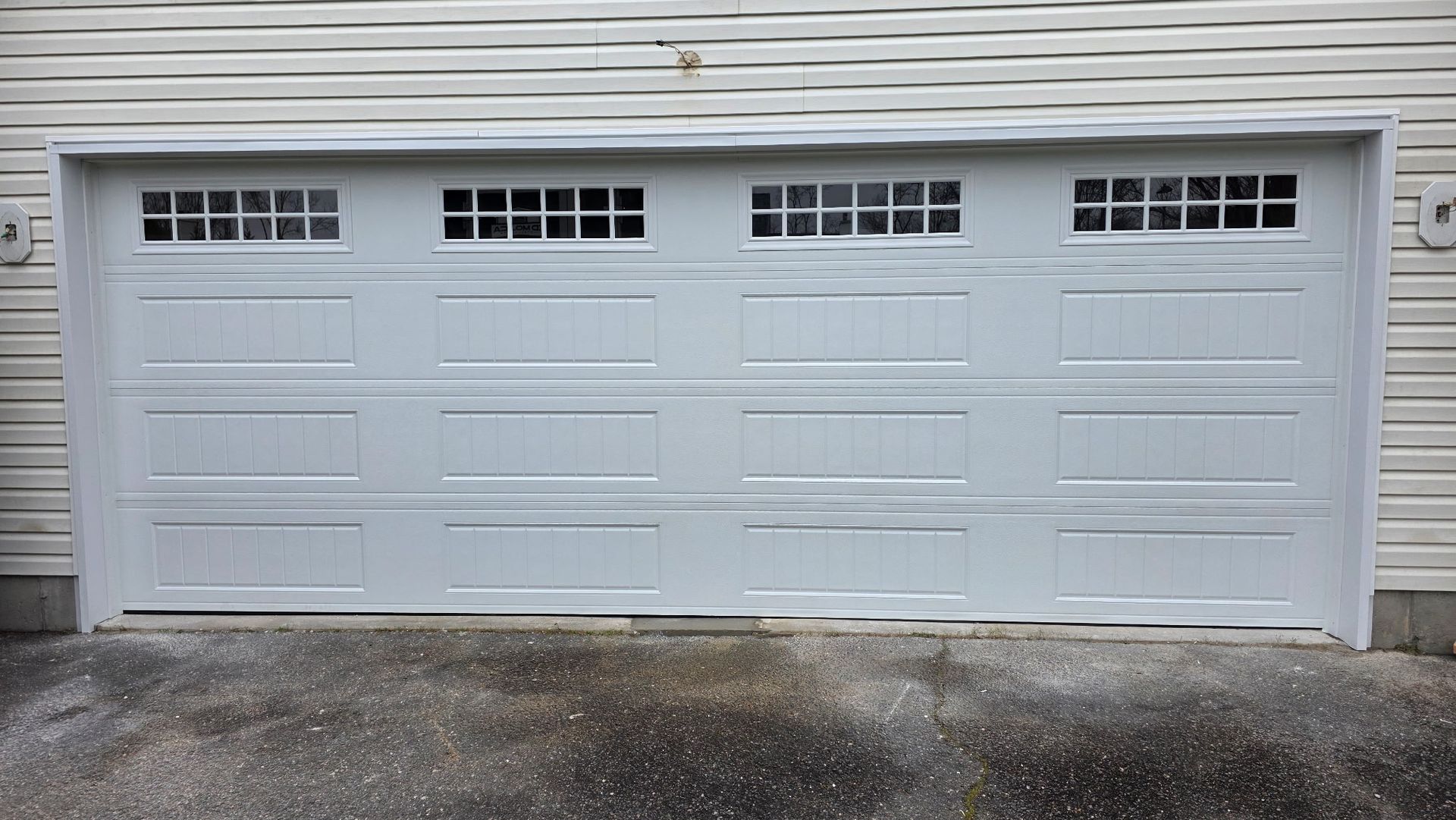 White garage door with four sections and small windows at the top, set in a house exterior.