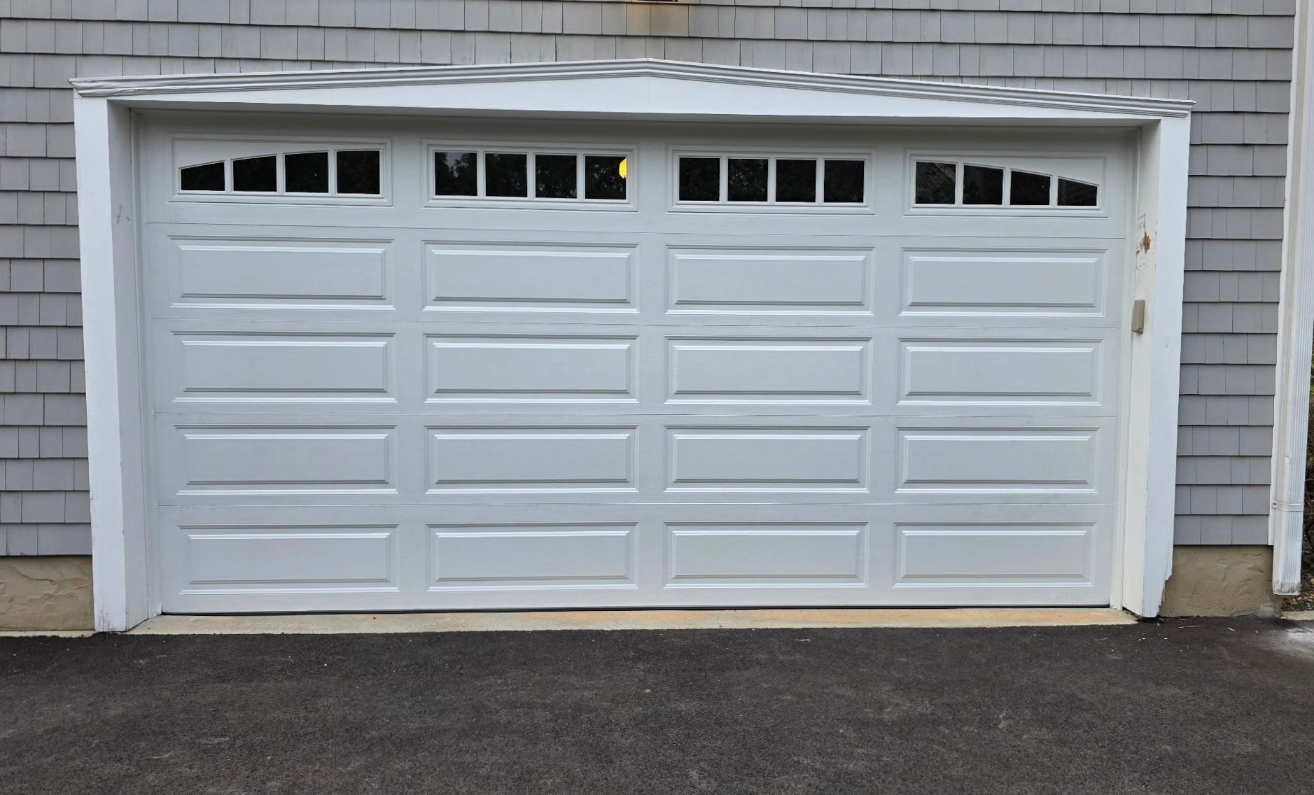 White triple-car garage door on a gray shingled house exterior, viewed from the driveway.
