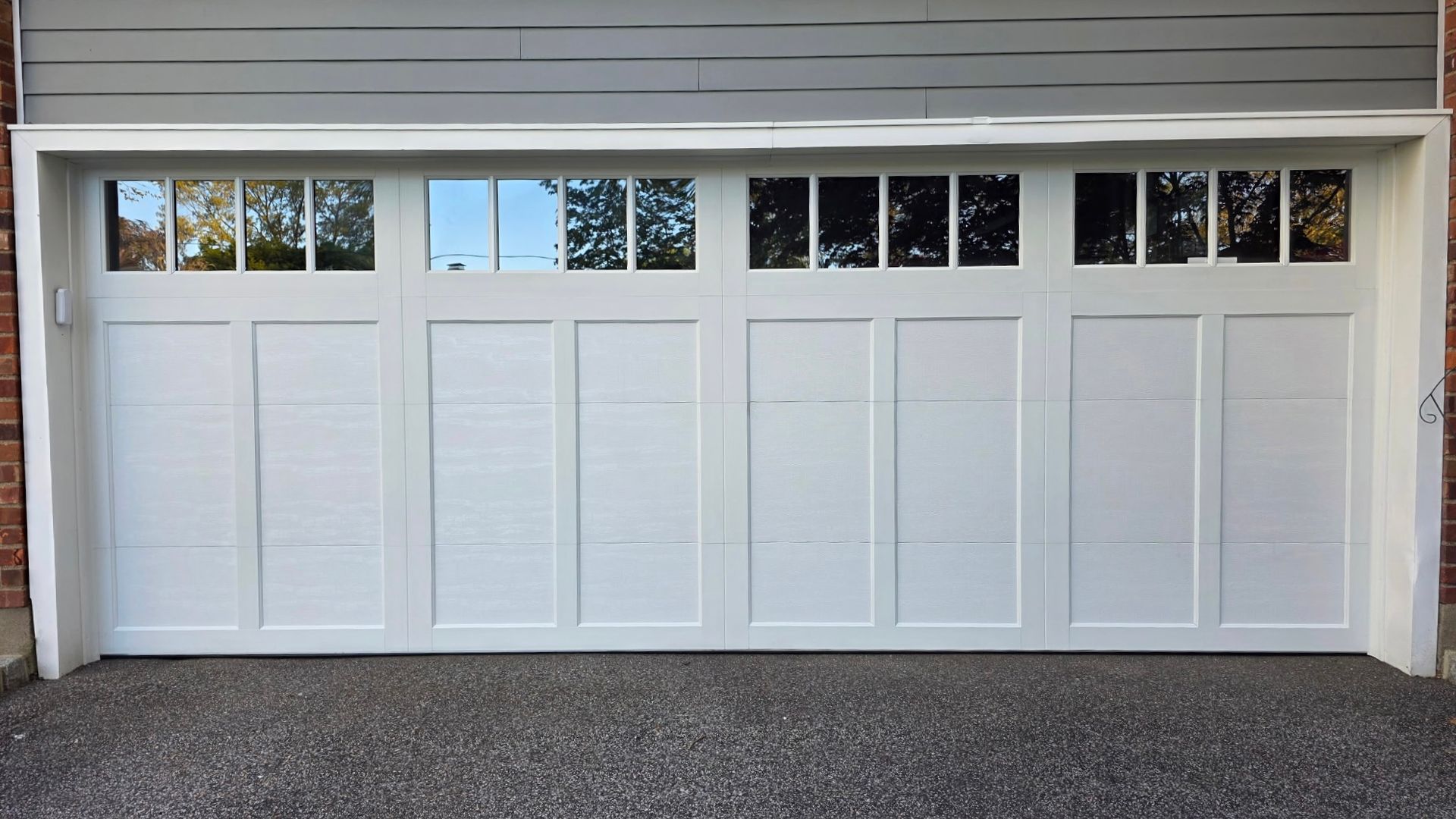 White multi-panel garage door with windows beneath gray siding and a gravel driveway