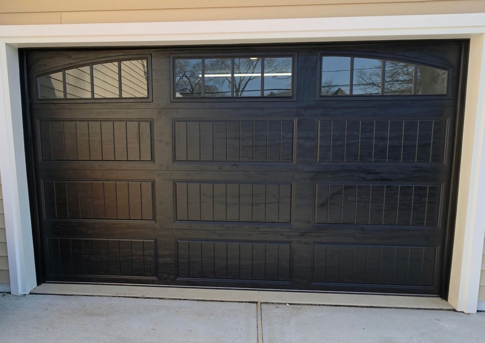 Black paneled garage door with small upper windows in a beige exterior wall