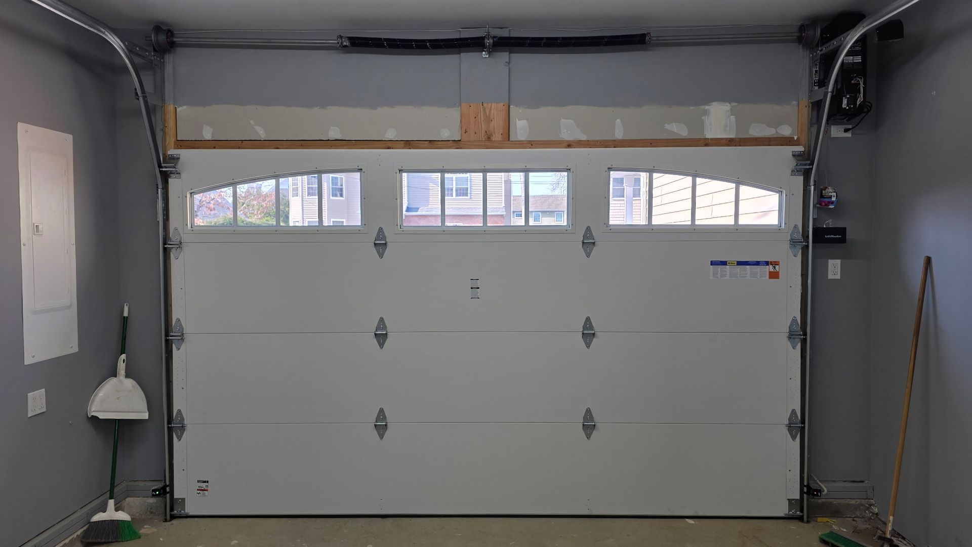 Interior of a garage with a closed white door, windows along the top, and cleaning tools at the sides