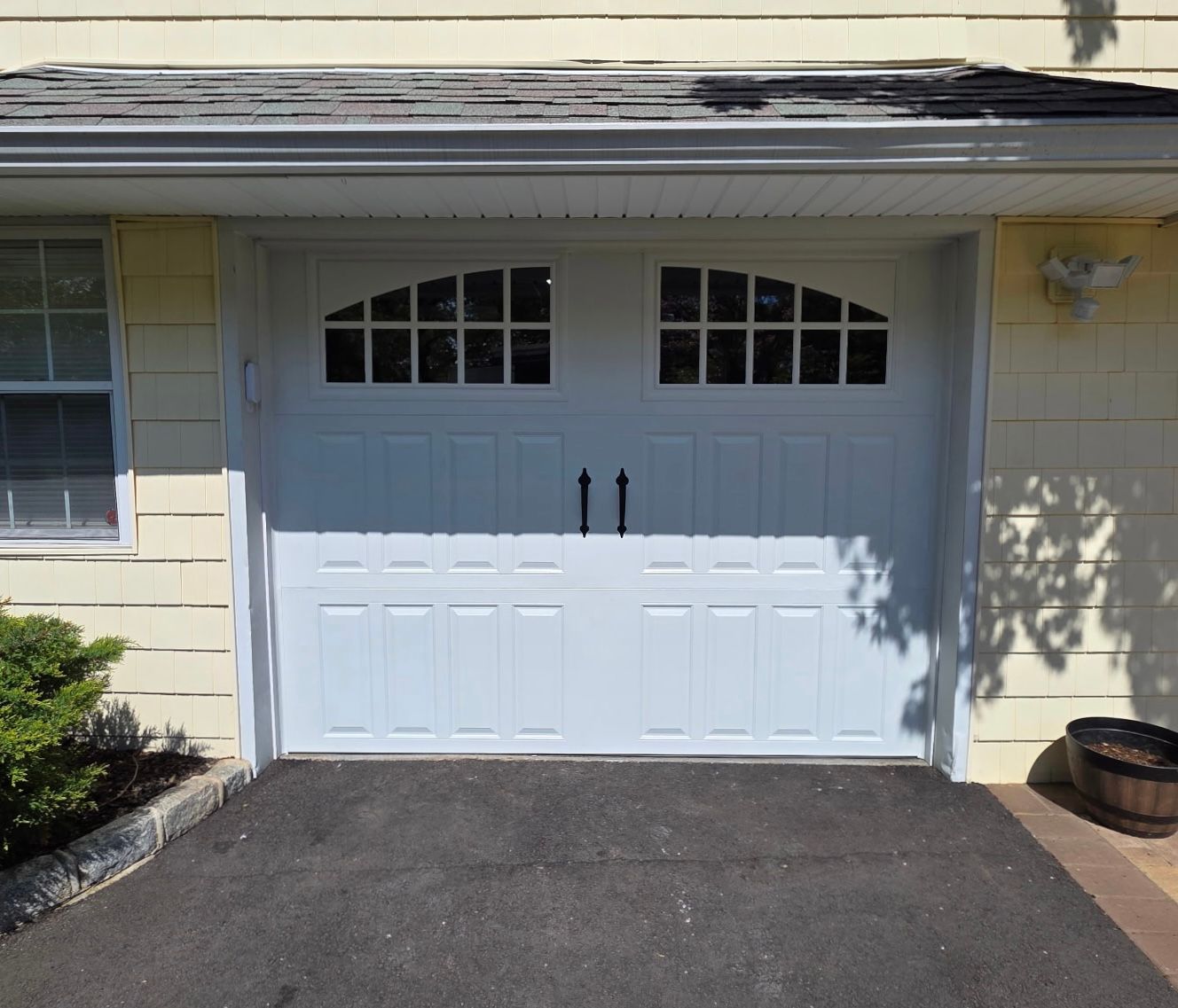 White two-car garage door with arched windows on a beige house exterior