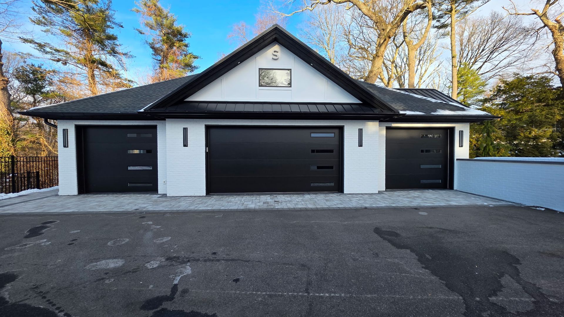 Modern single-story house with three black garage doors and a paved driveway in front