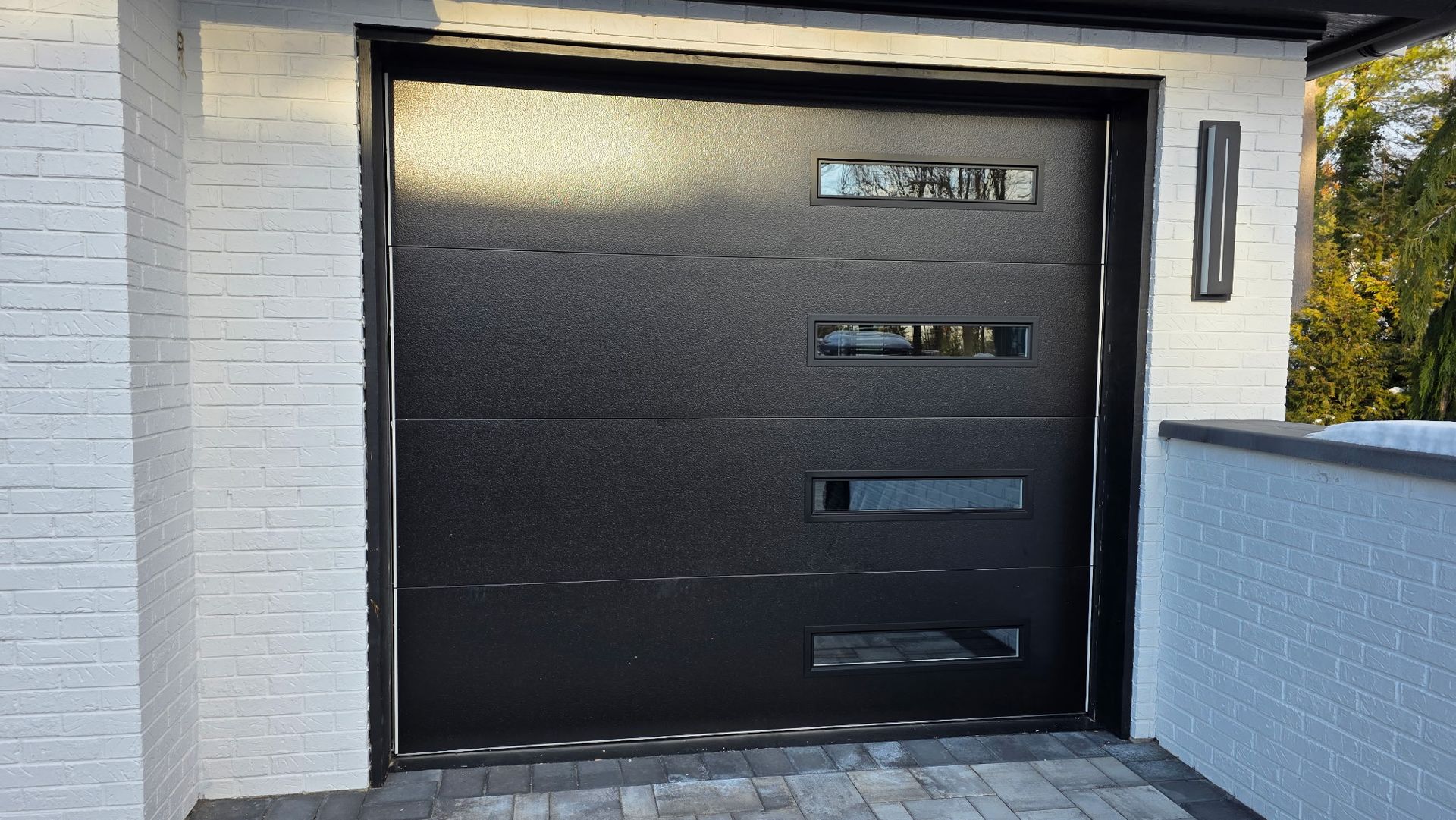 Modern black front garage door with narrow horizontal windows set in a white exterior wall