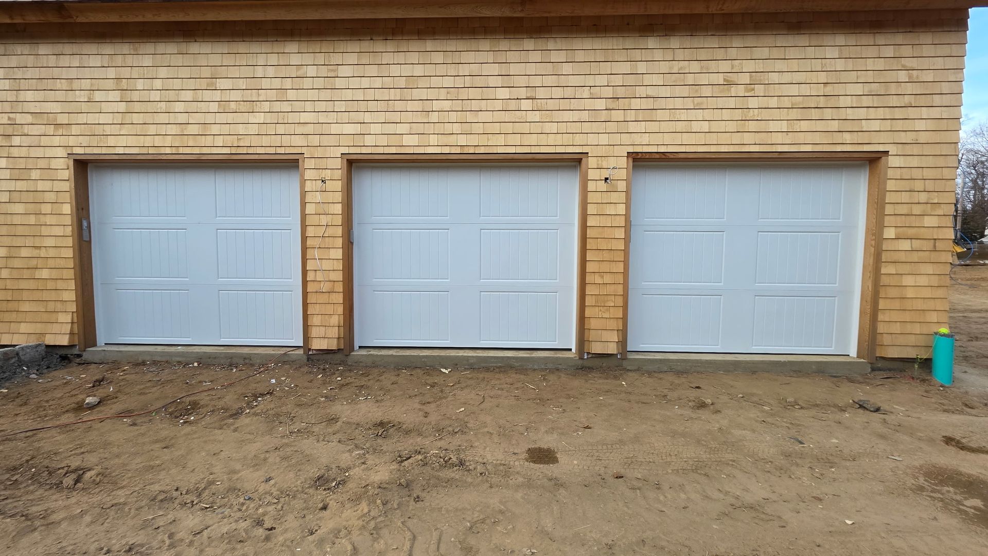 Three light gray garage doors in a tan brick building with bare dirt foreground.