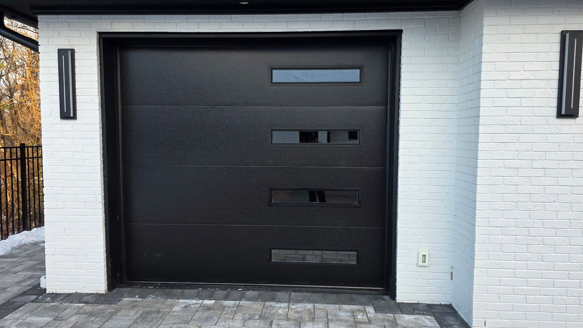 Modern black garage door with horizontal windows set in a white brick exterior
