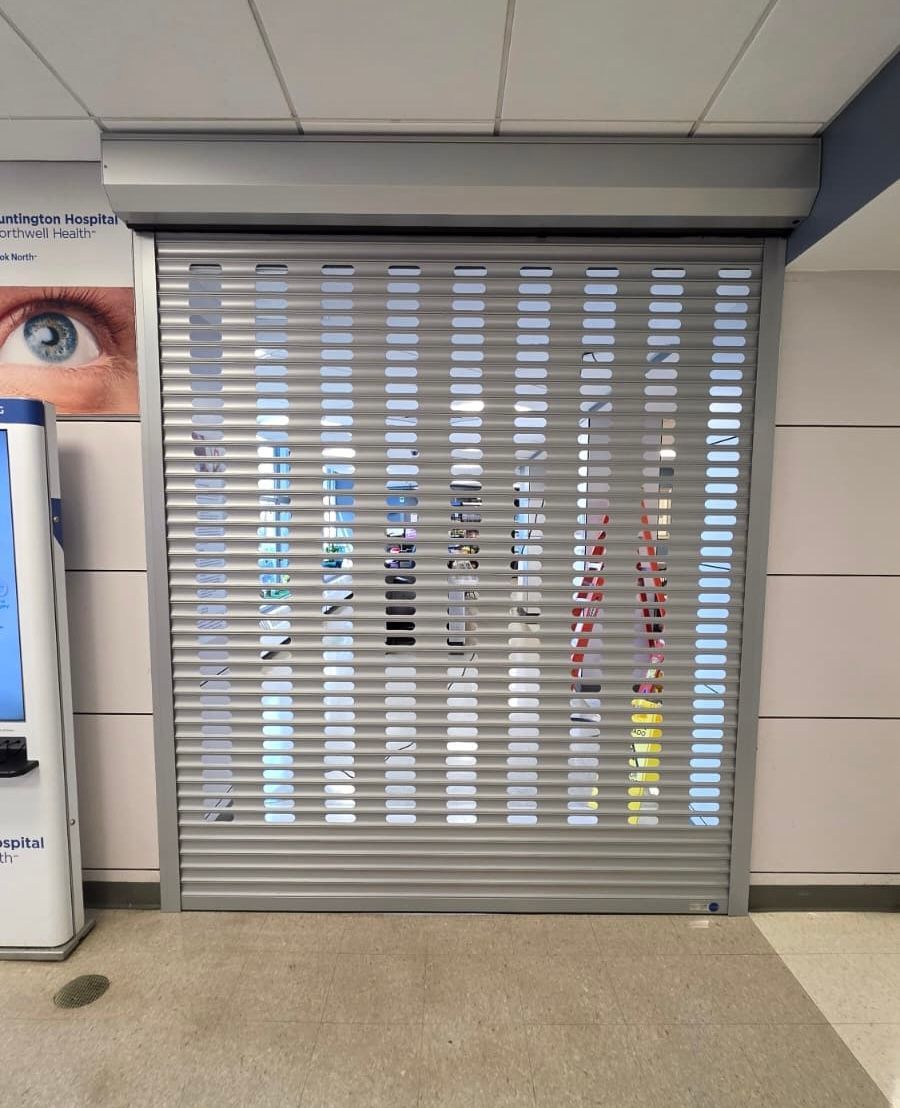 Closed metal storefront shutter in a hallway, with a partial wall graphic and floor markings visible on the sides