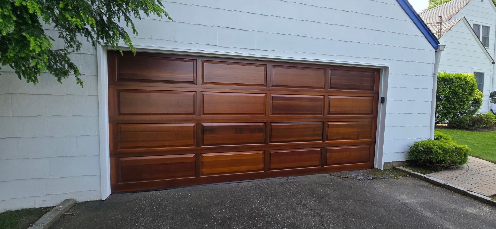 Brown wooden garage door on a white house exterior with driveway in front
