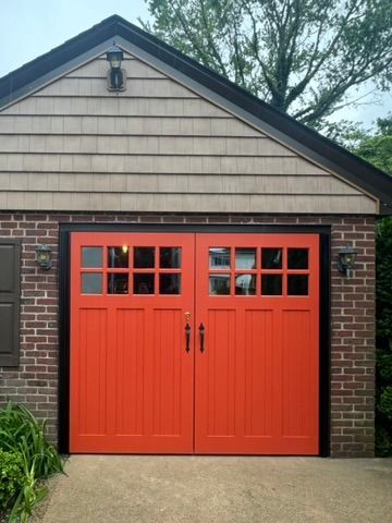 Orange double garage doors on a brick garage with beige siding and a small window panel above each door