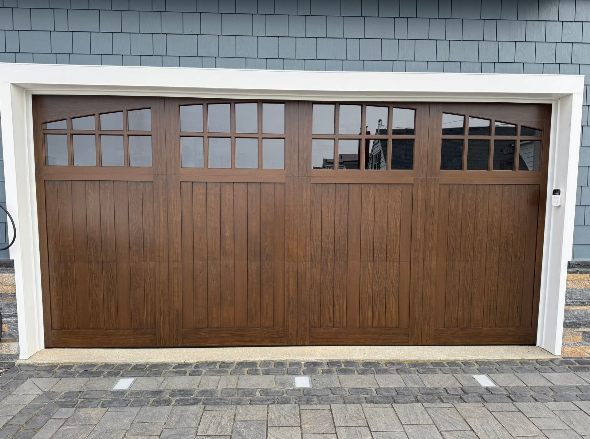 Wooden two-car garage door with small windows, set in a gray brick exterior wall.