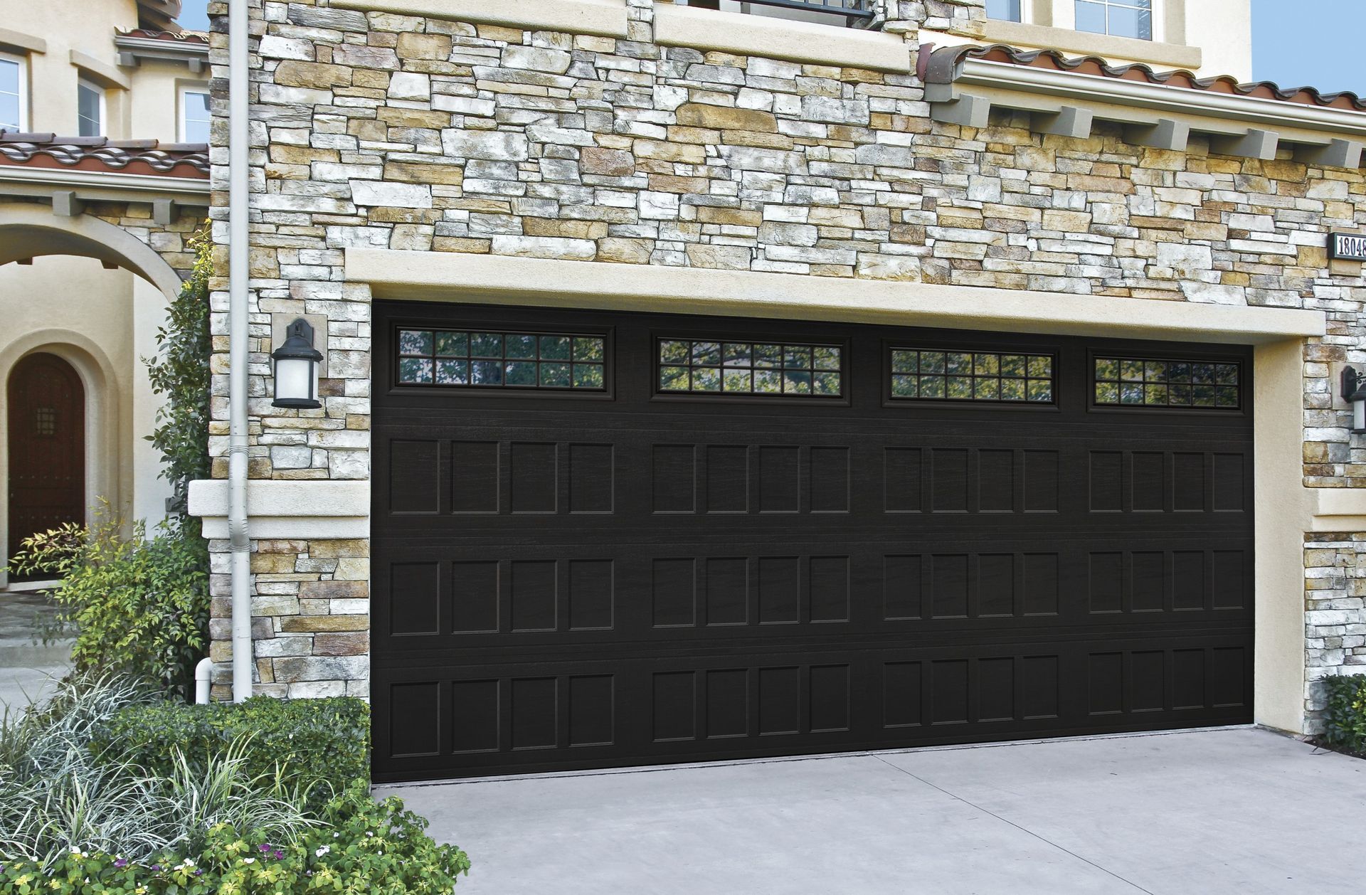 Dark brown garage door with windowed top and stone exterior.