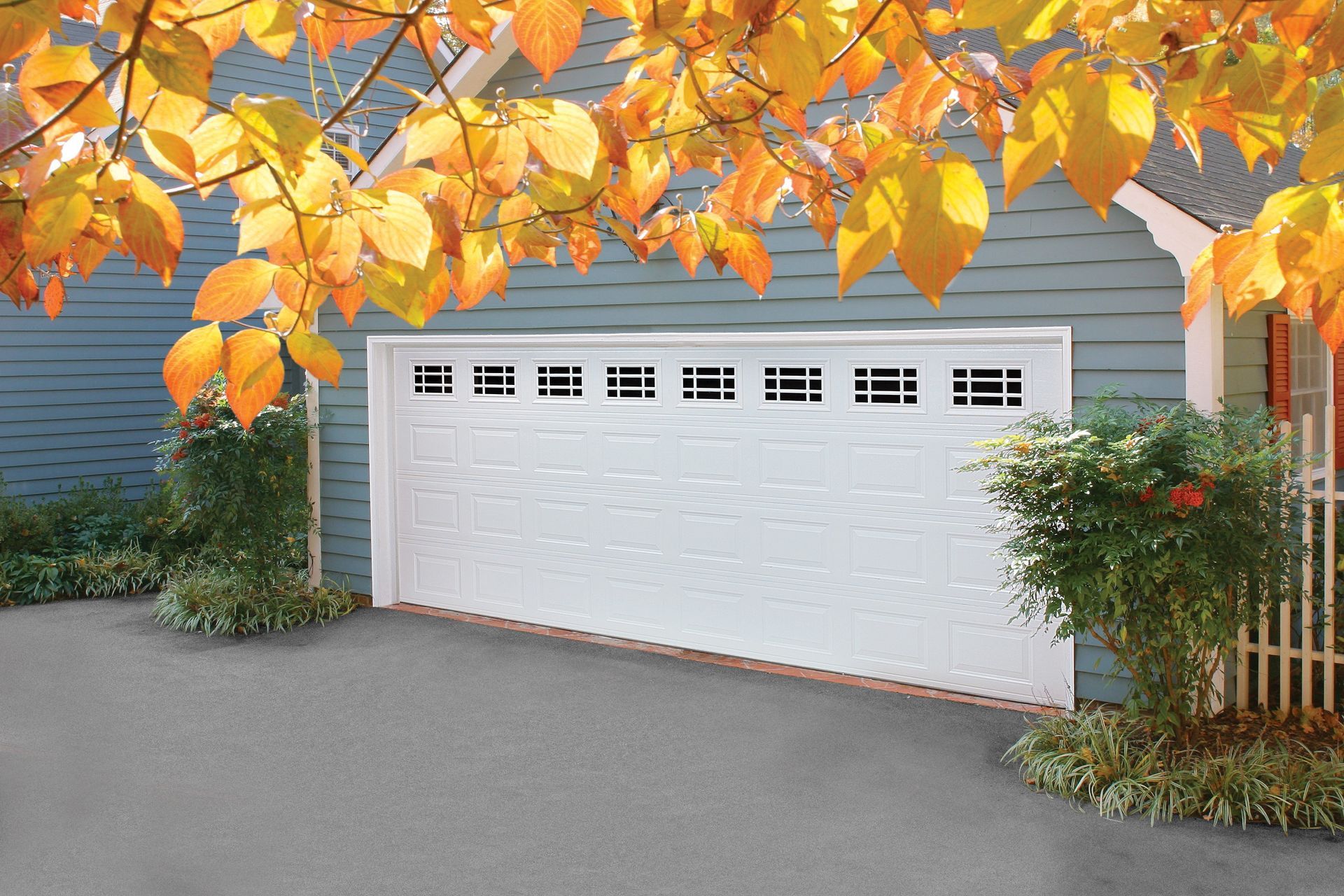 White garage door with windows, on a blue house, under fall foliage.