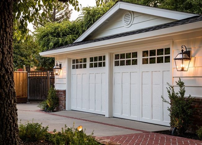 Two wooden garage doors with black lantern lights on a white house exterior
