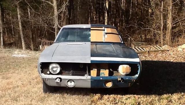 Half-painted classic car parked on grass in a wooded area, split gray and black with orange primer patches