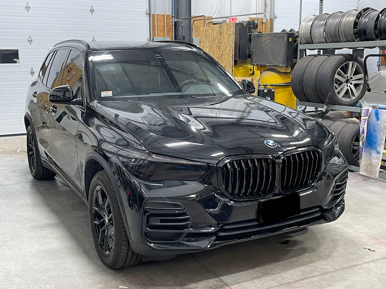A black bmw x5 is parked in a garage next to tires.