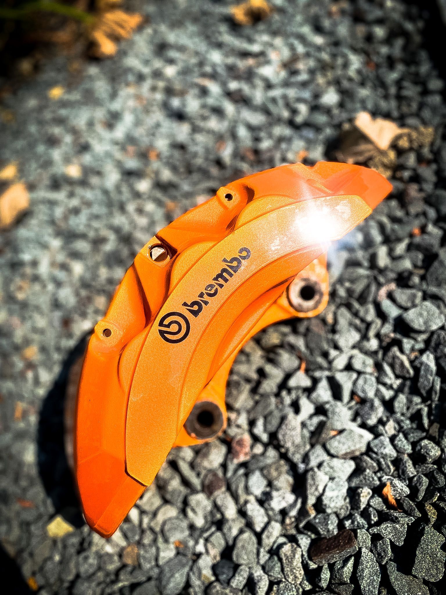 A close up of a brembo brake caliper on a rocky surface.