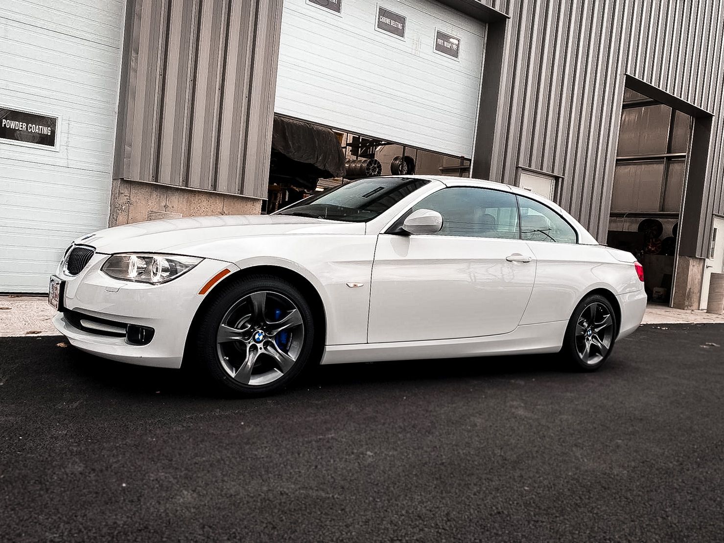 A white bmw is parked in front of a garage door.