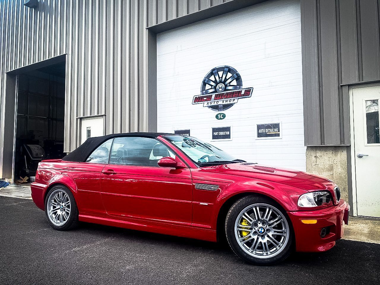 A red bmw m3 convertible is parked in front of a garage door.