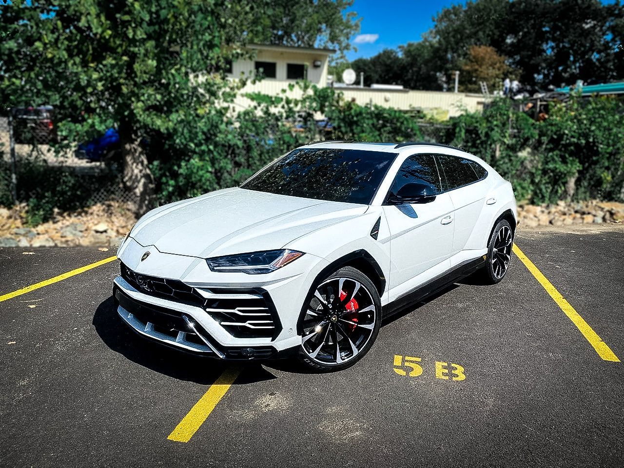 A white lamborghini urus is parked in a parking lot.