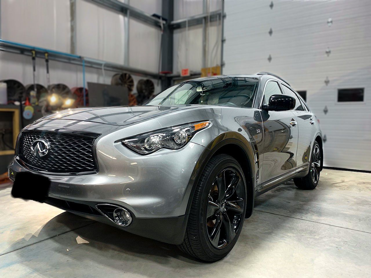 A silver infiniti qx70 is parked in a garage next to a garage door.
