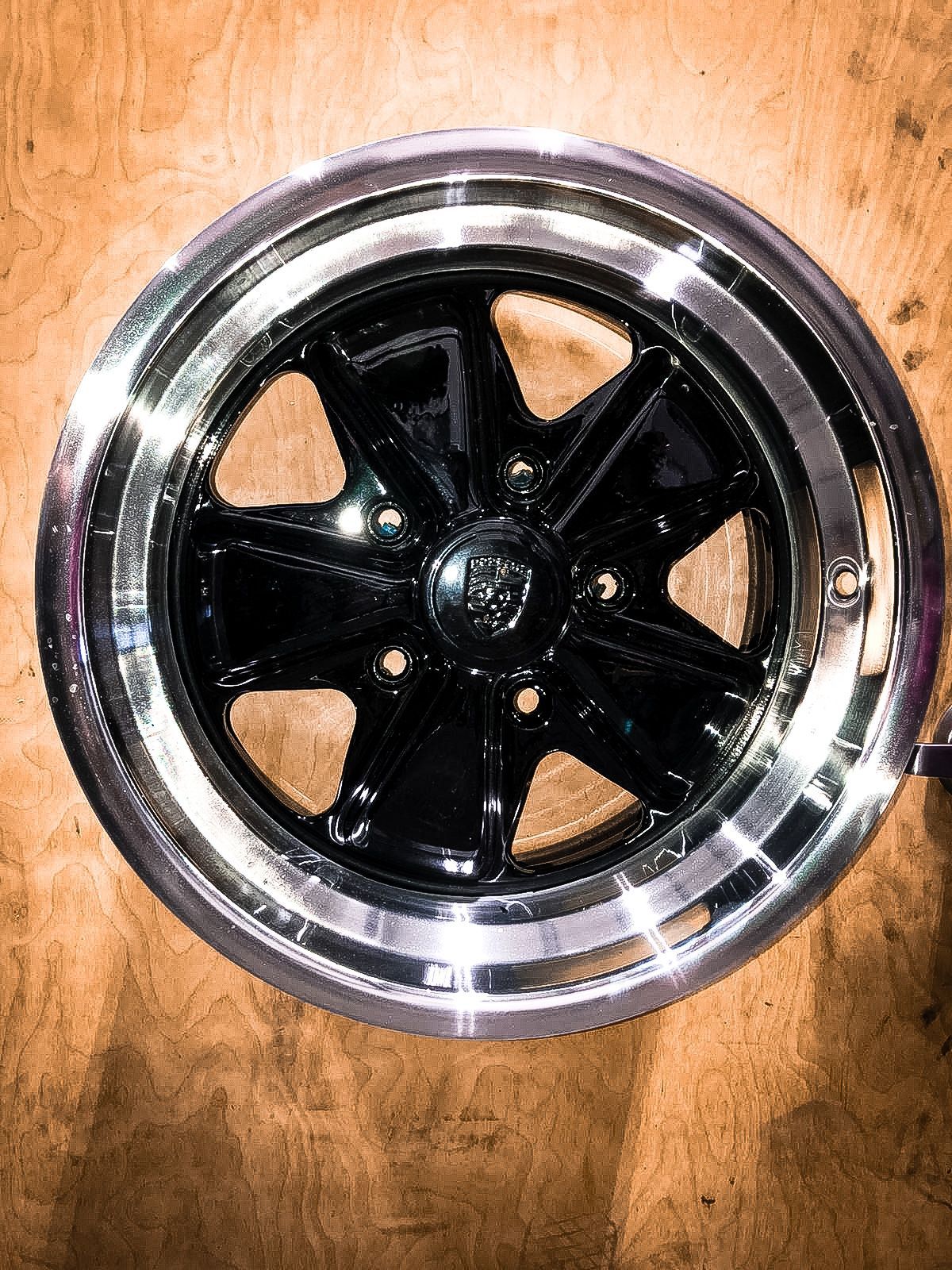 A black wheel with a chrome rim is sitting on a wooden table.