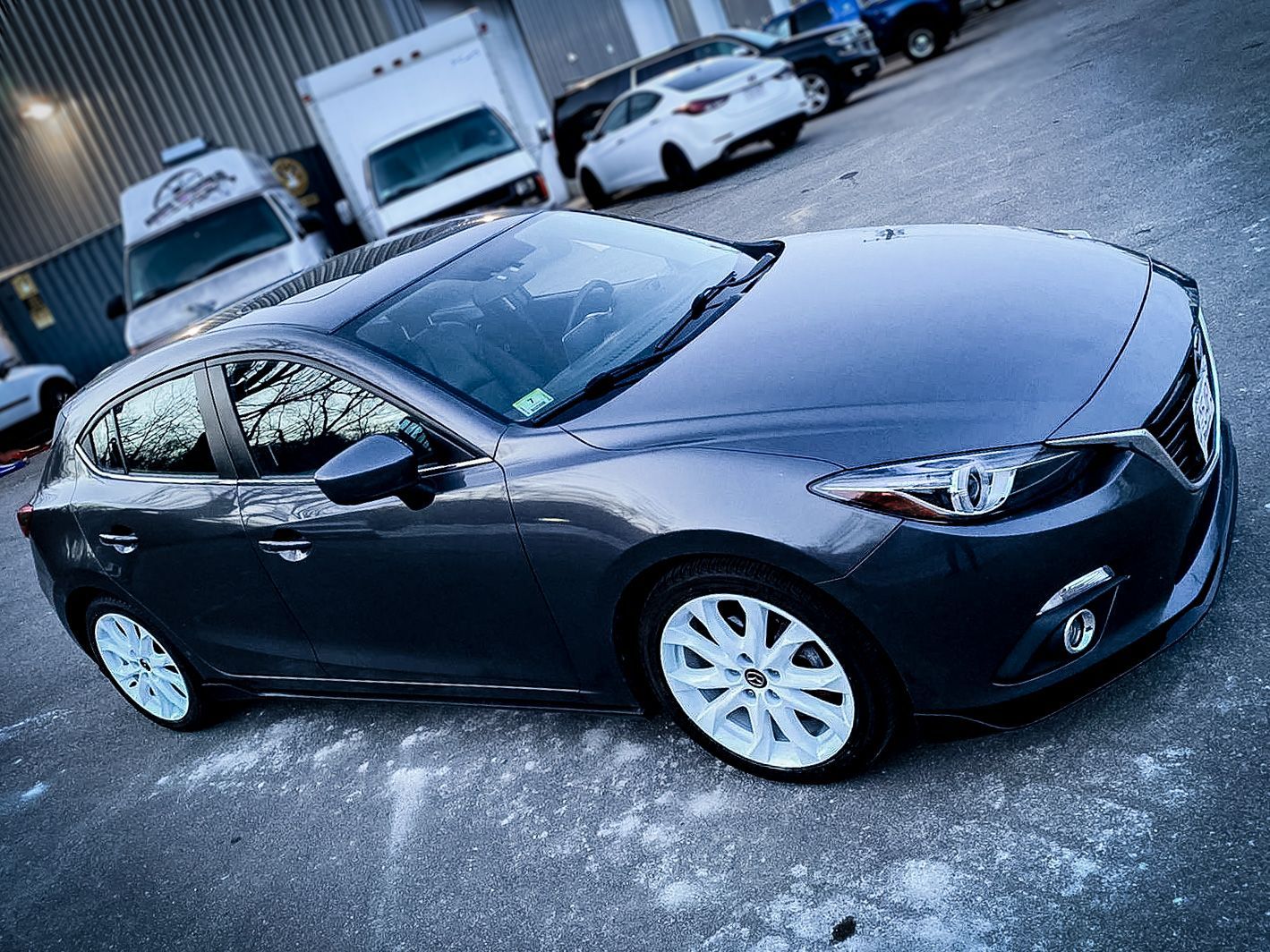 A gray car is parked in a parking lot in front of a building.