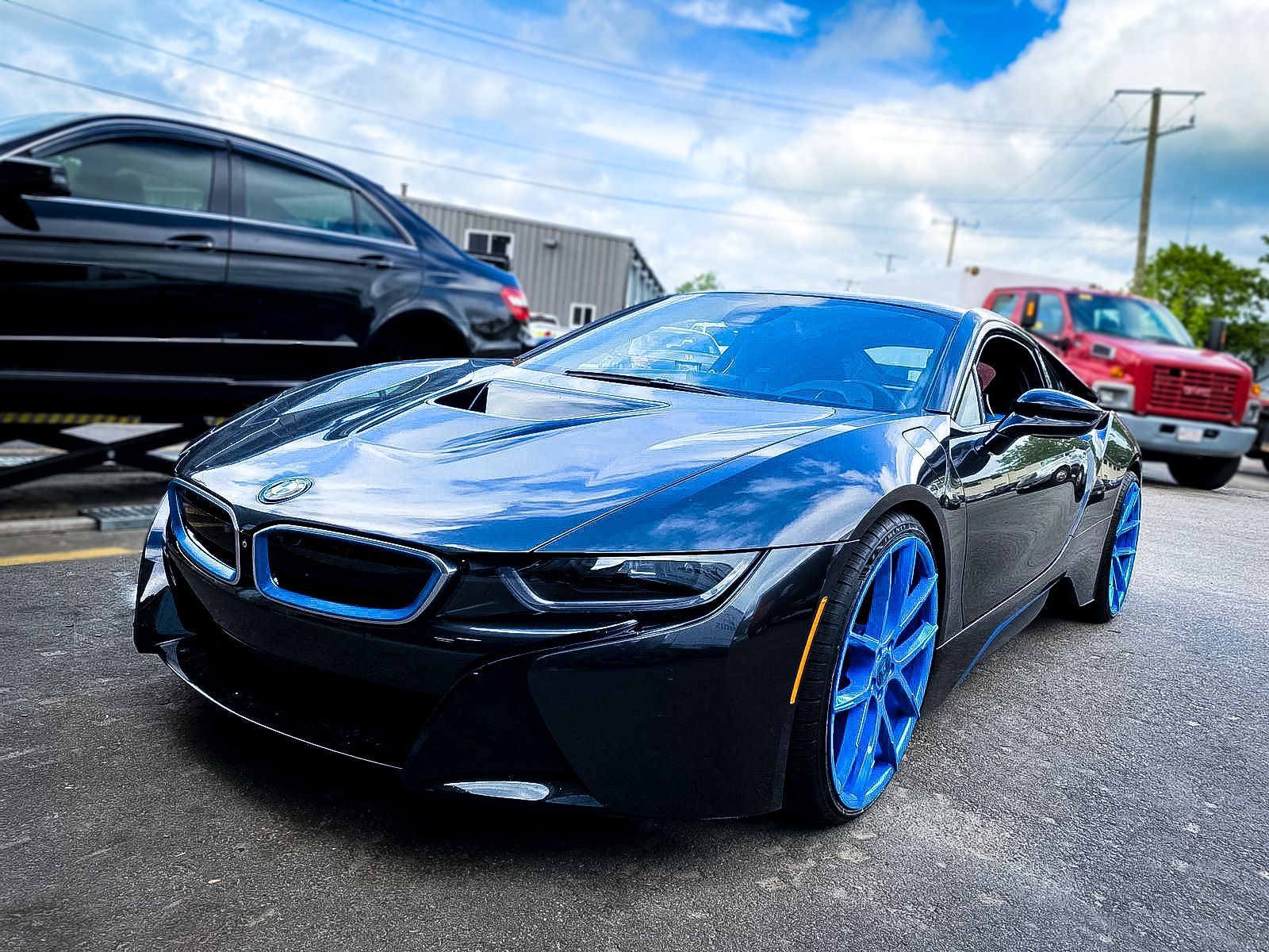 A black bmw i8 with blue wheels is parked on the side of the road.