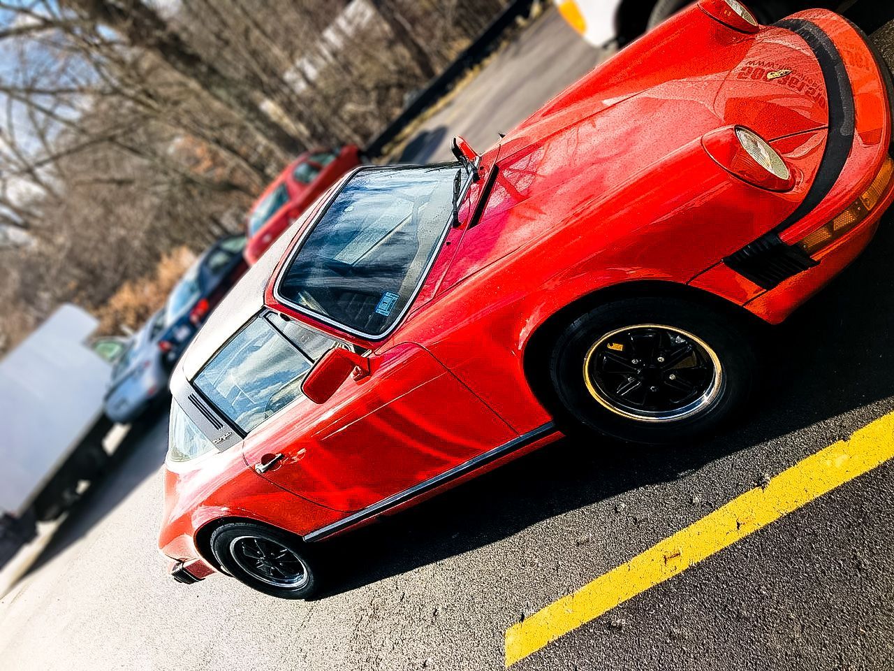 A red car is parked in a parking lot next to a yellow line