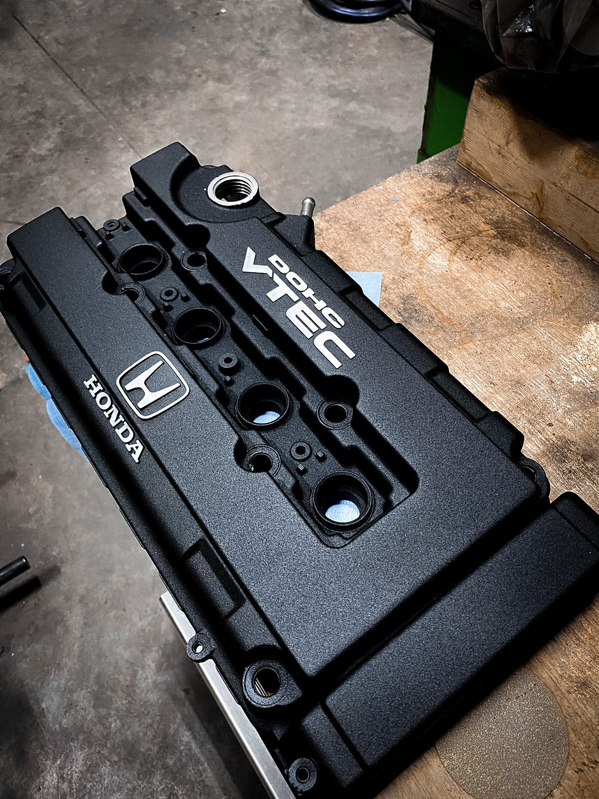 A black honda vtec engine cover is sitting on top of a wooden table.