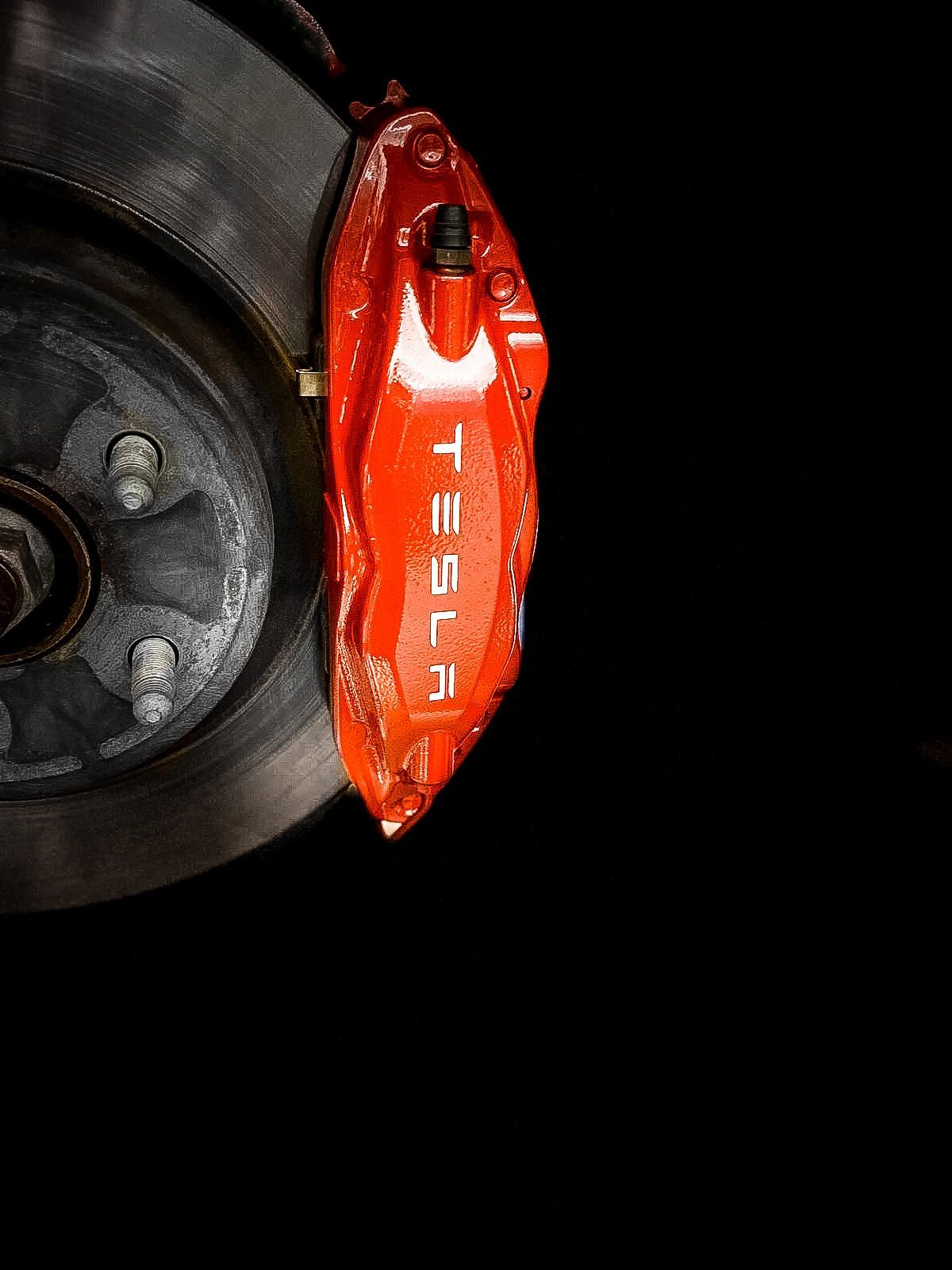 A close up of a tesla brake caliper on a black background.