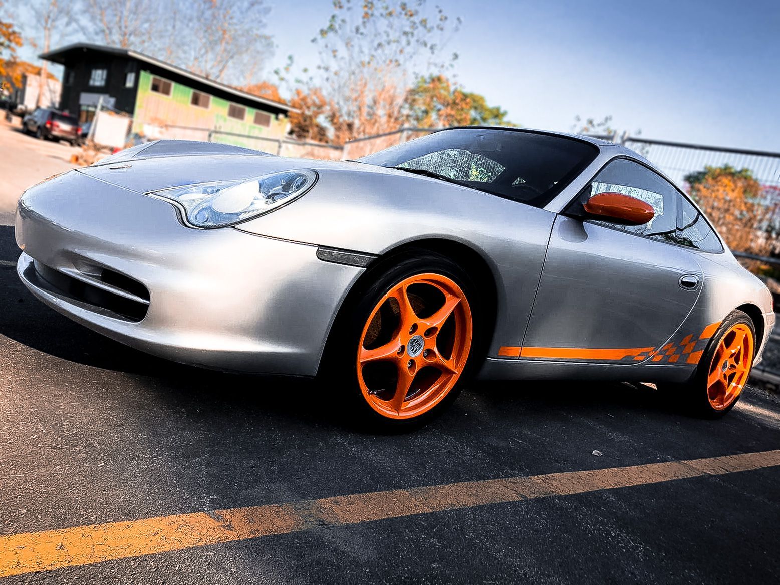 A silver sports car with orange wheels is parked in a parking lot