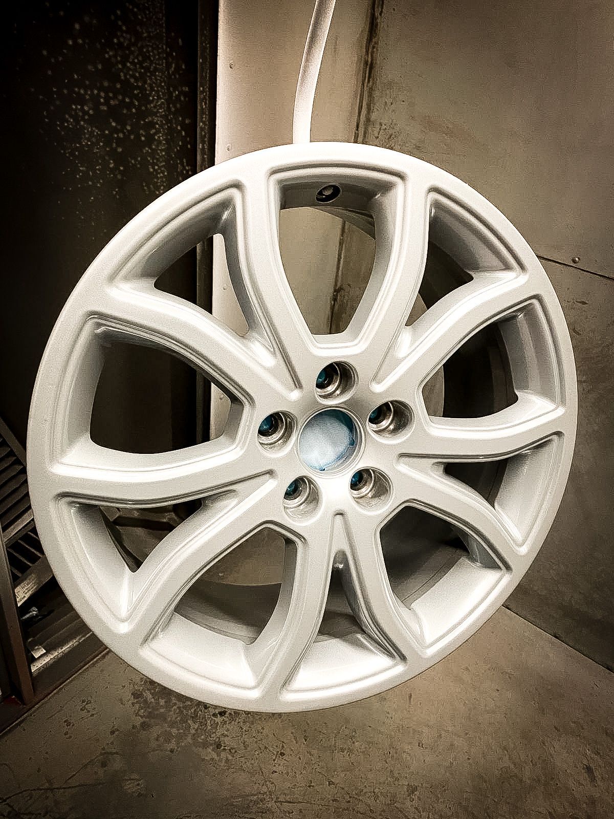A white car wheel is sitting on a concrete floor.