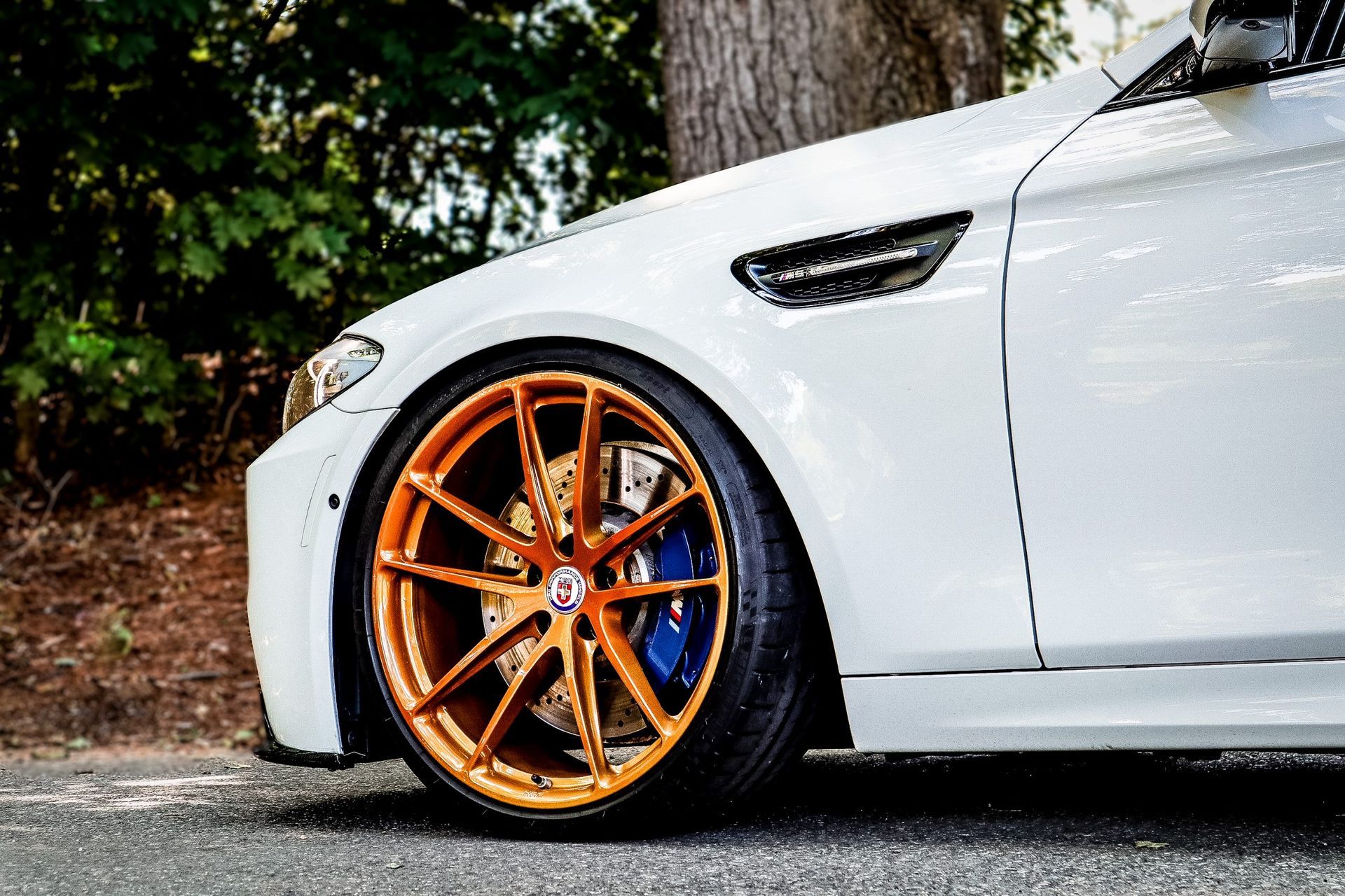A white car with orange wheels and blue brake calipers is parked on the side of the road.