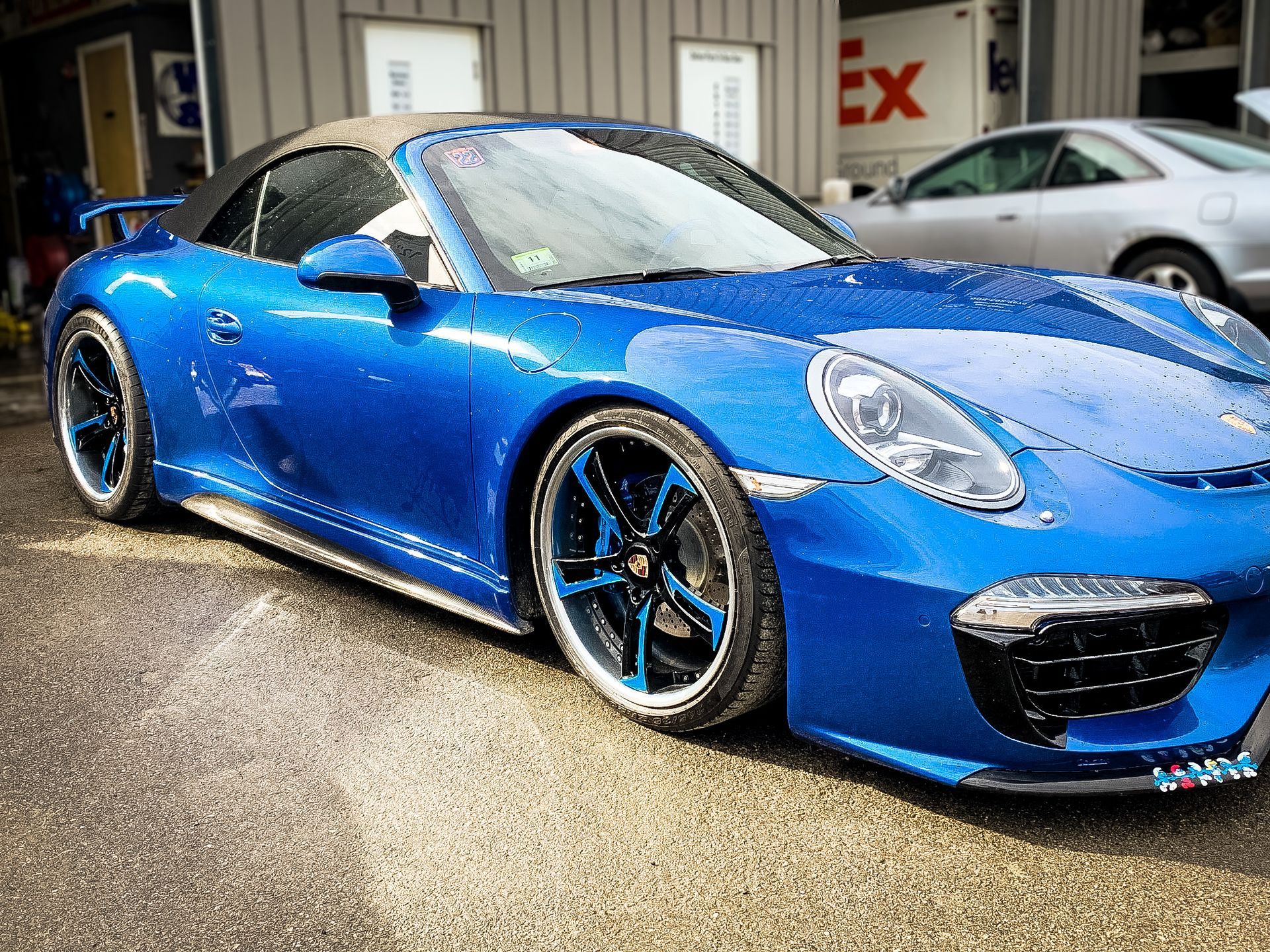 A blue porsche 911 convertible is parked in front of a building.
