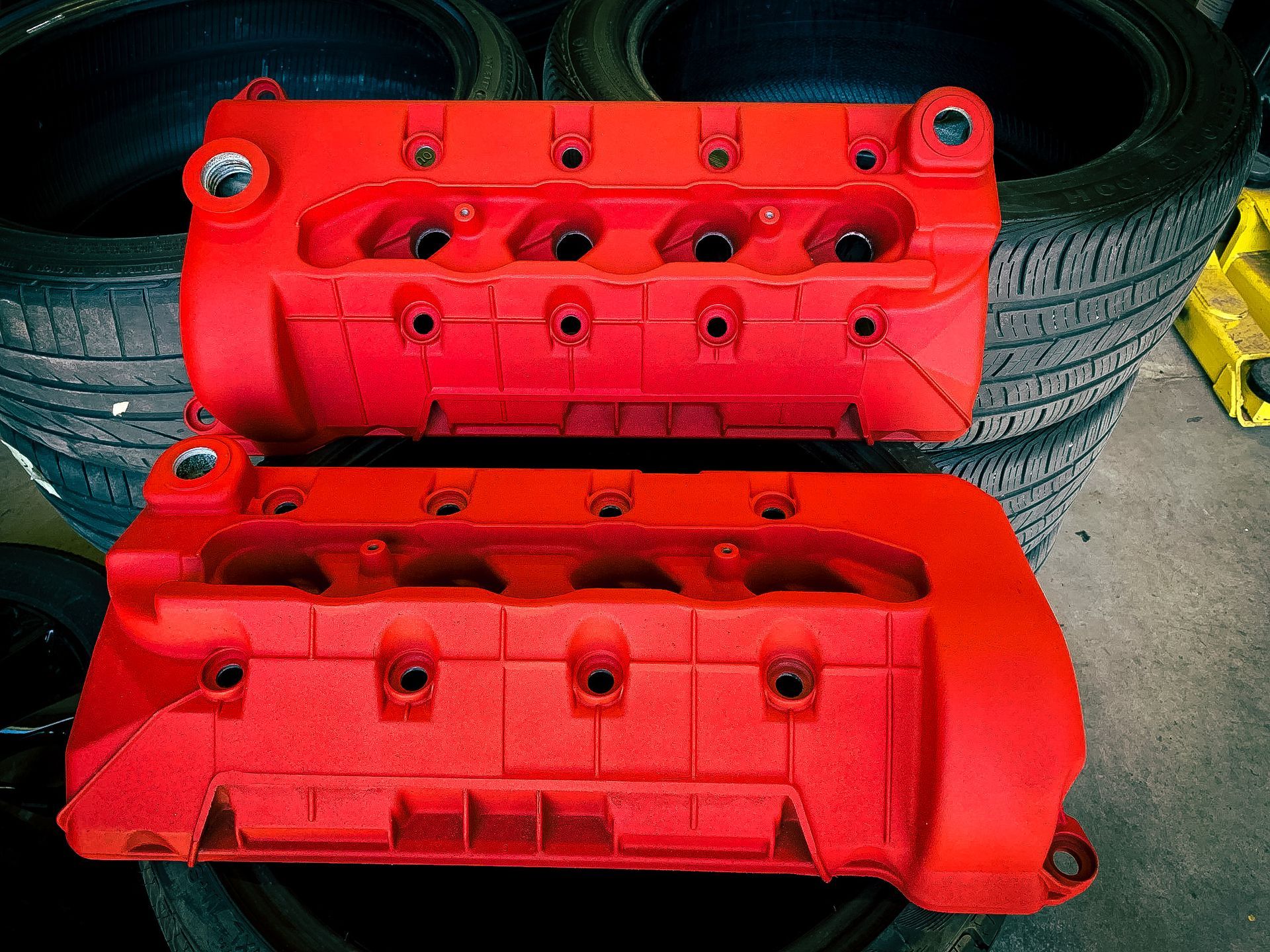 A pair of red valve covers are sitting on top of a pile of tires.