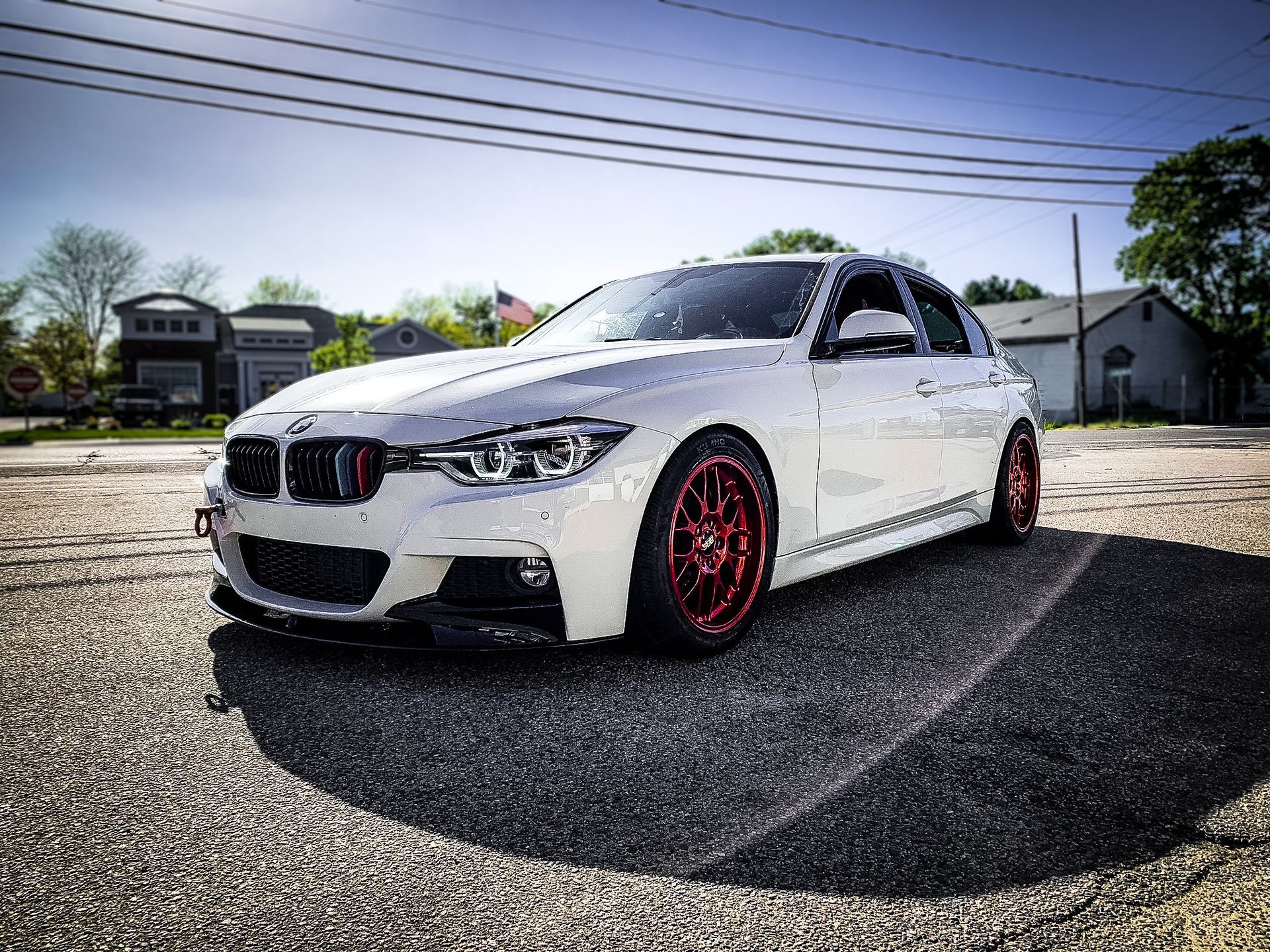 A white bmw with red wheels is parked on the side of the road.