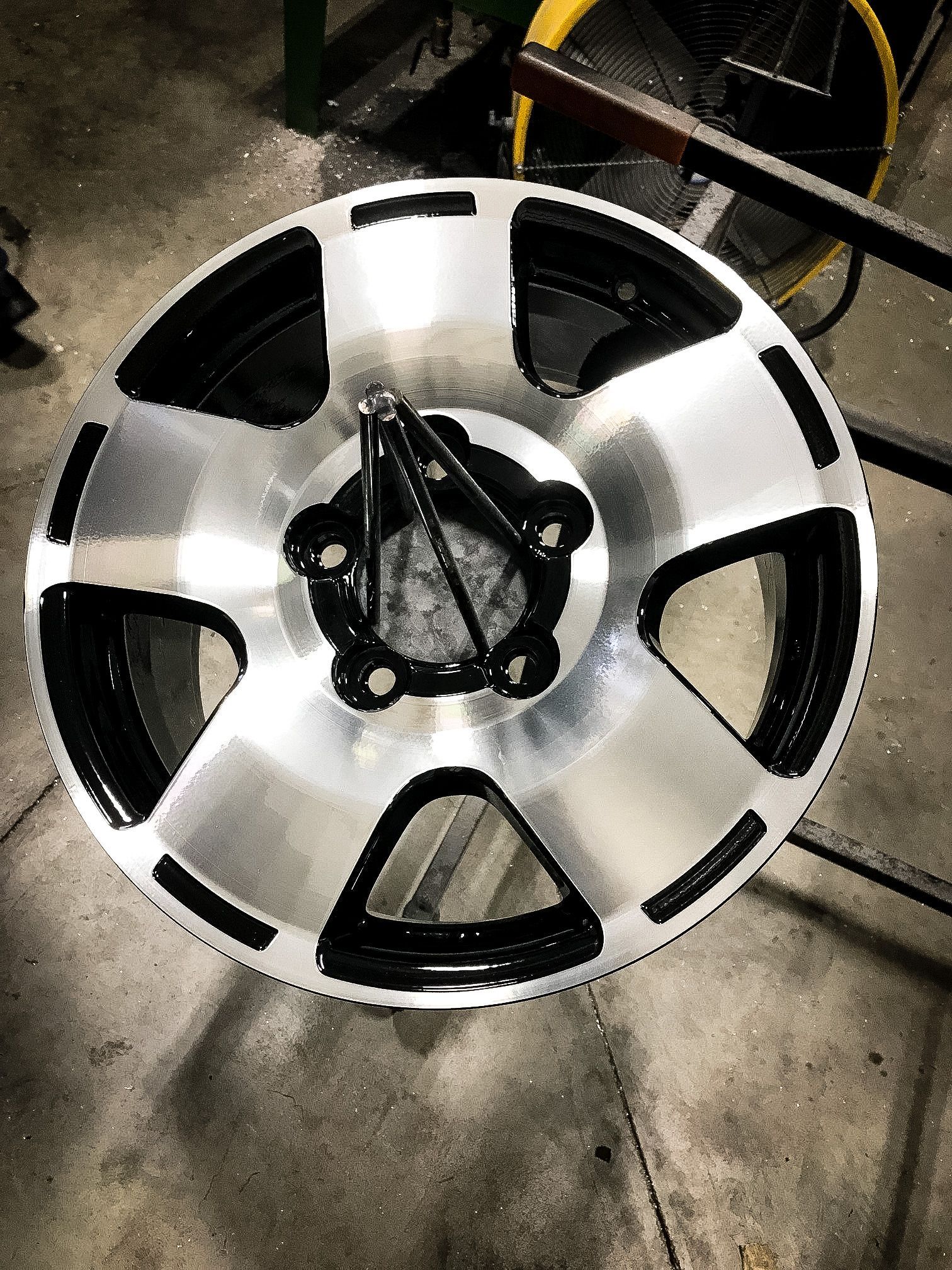 A silver and black wheel is sitting on a concrete floor.