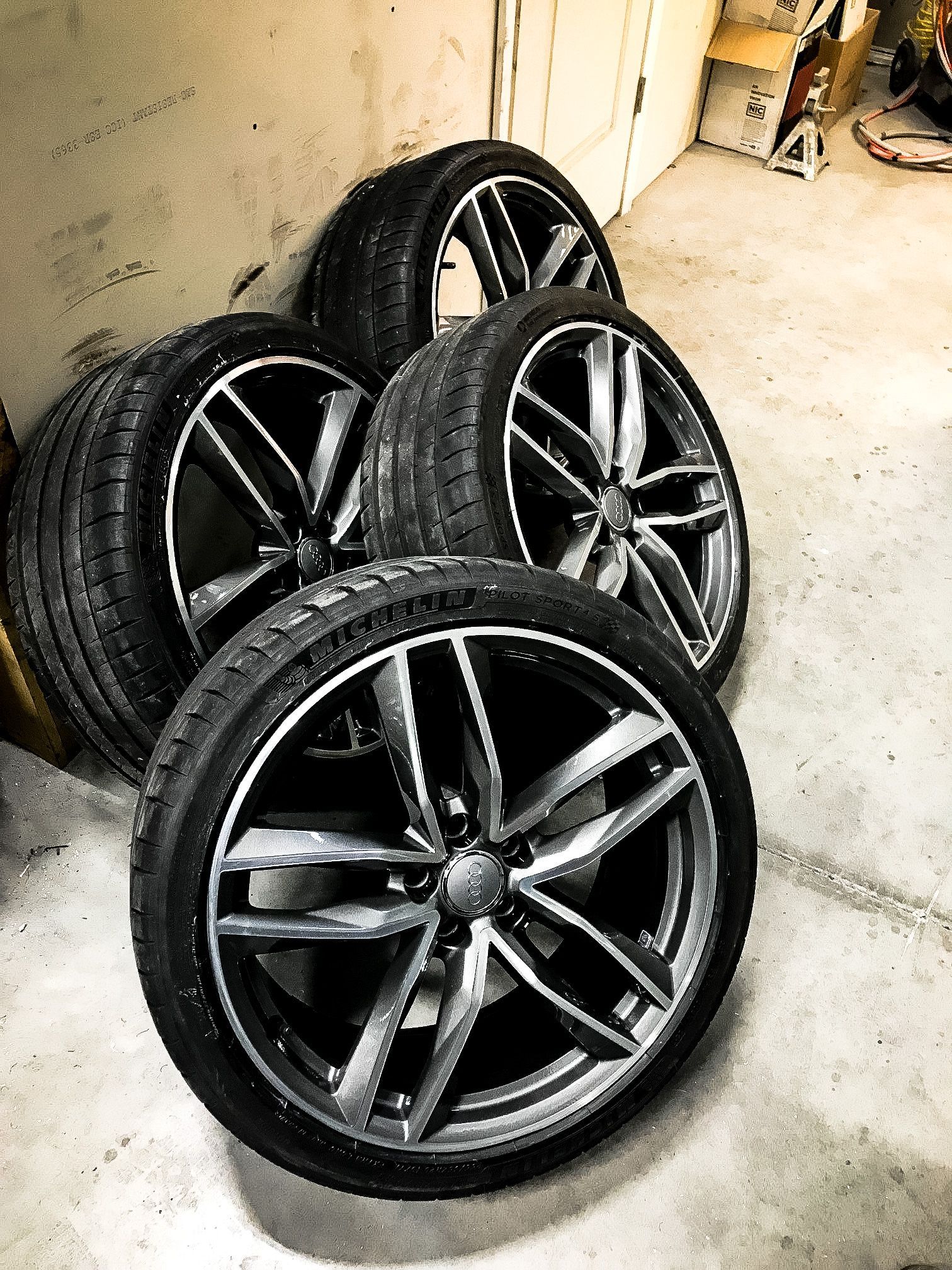 A bunch of tires and wheels are stacked on top of each other in a garage.